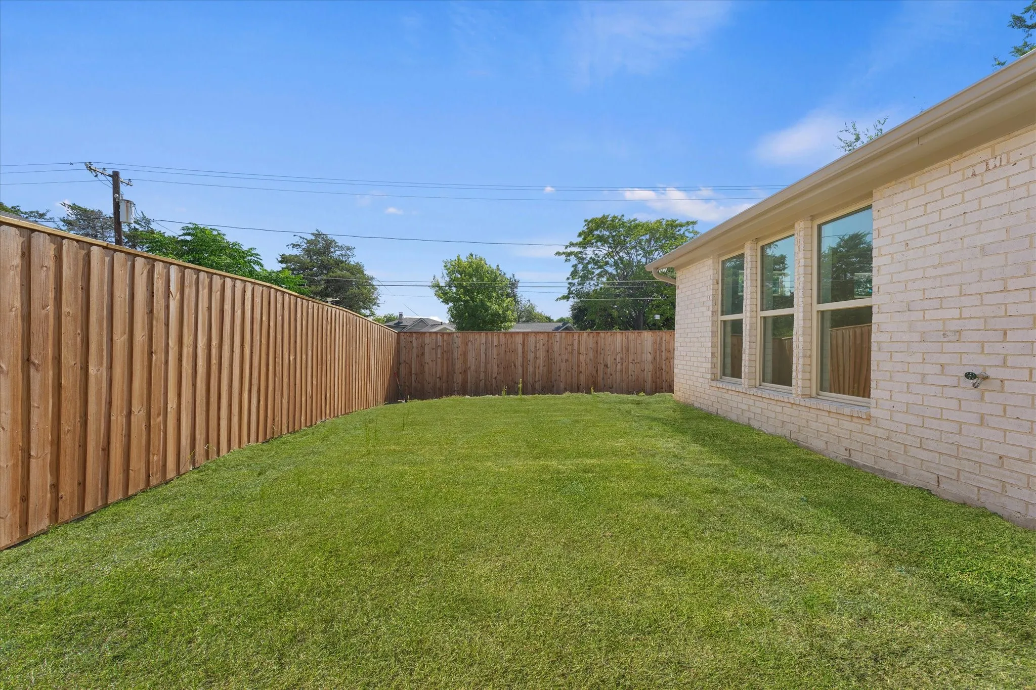 Expansive grassy yard with a wood privacy fence and a brick-finish exterior