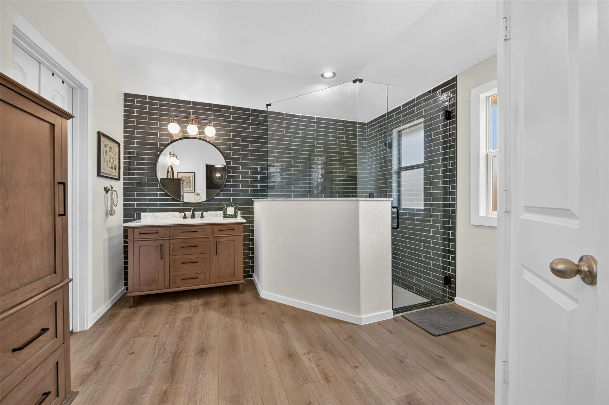 Wood-finish flooring with a wood vanity, white countertop, and dark subway tile accent wall
