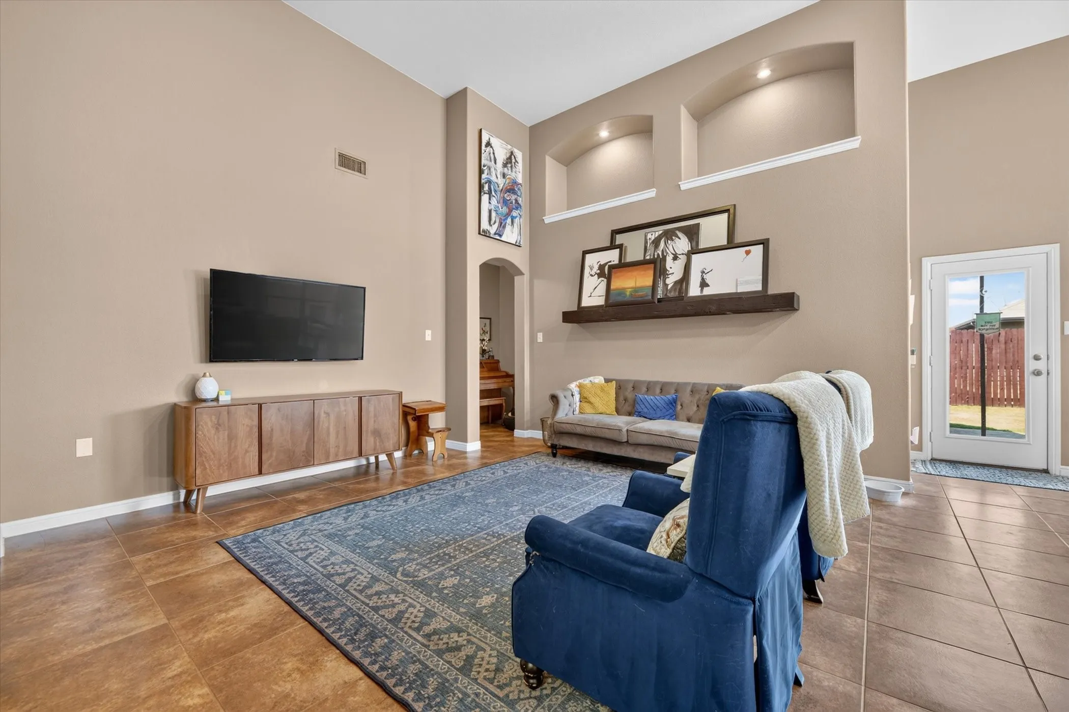 Vaulted ceilings, archway, recessed wall niches with accent lighting, and a glass-paneled exterior door