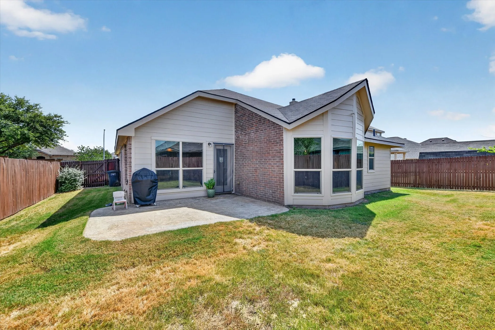 Rear exterior with a concrete patio, brick and siding facade, multiple large windows, and a fenced backyard