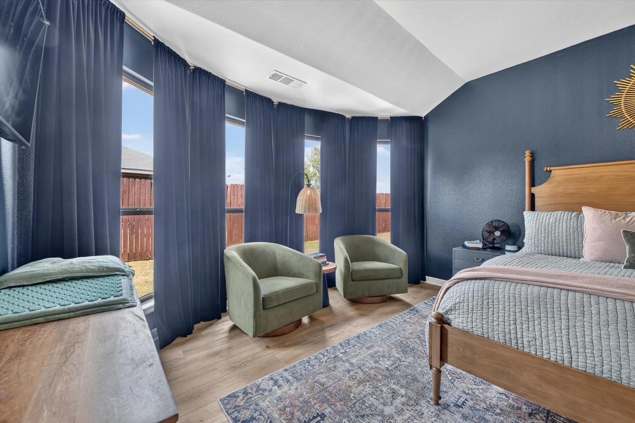 Vaulted ceiling, wood-finish flooring, multiple windows with full-length drapery, and a wood bed frame