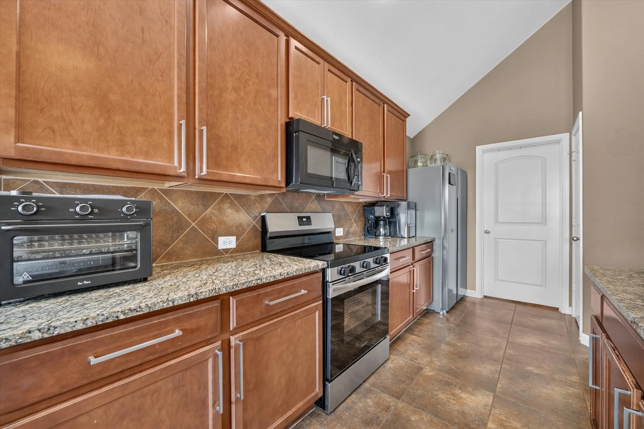 Vaulted ceiling, wood cabinetry, granite countertops, tile backsplash, and stainless steel appliances