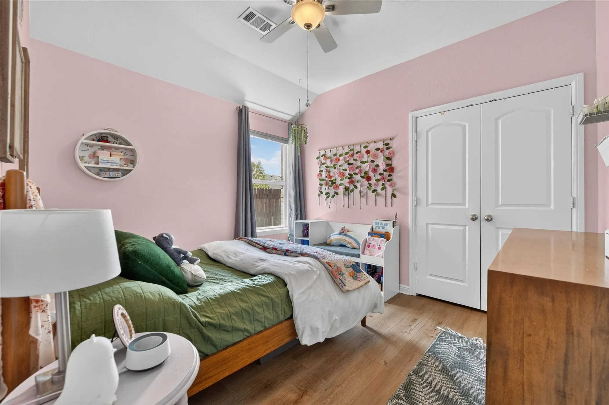 Wood-finish flooring, ceiling fan with integrated lighting, window with curtains, and double-door closet