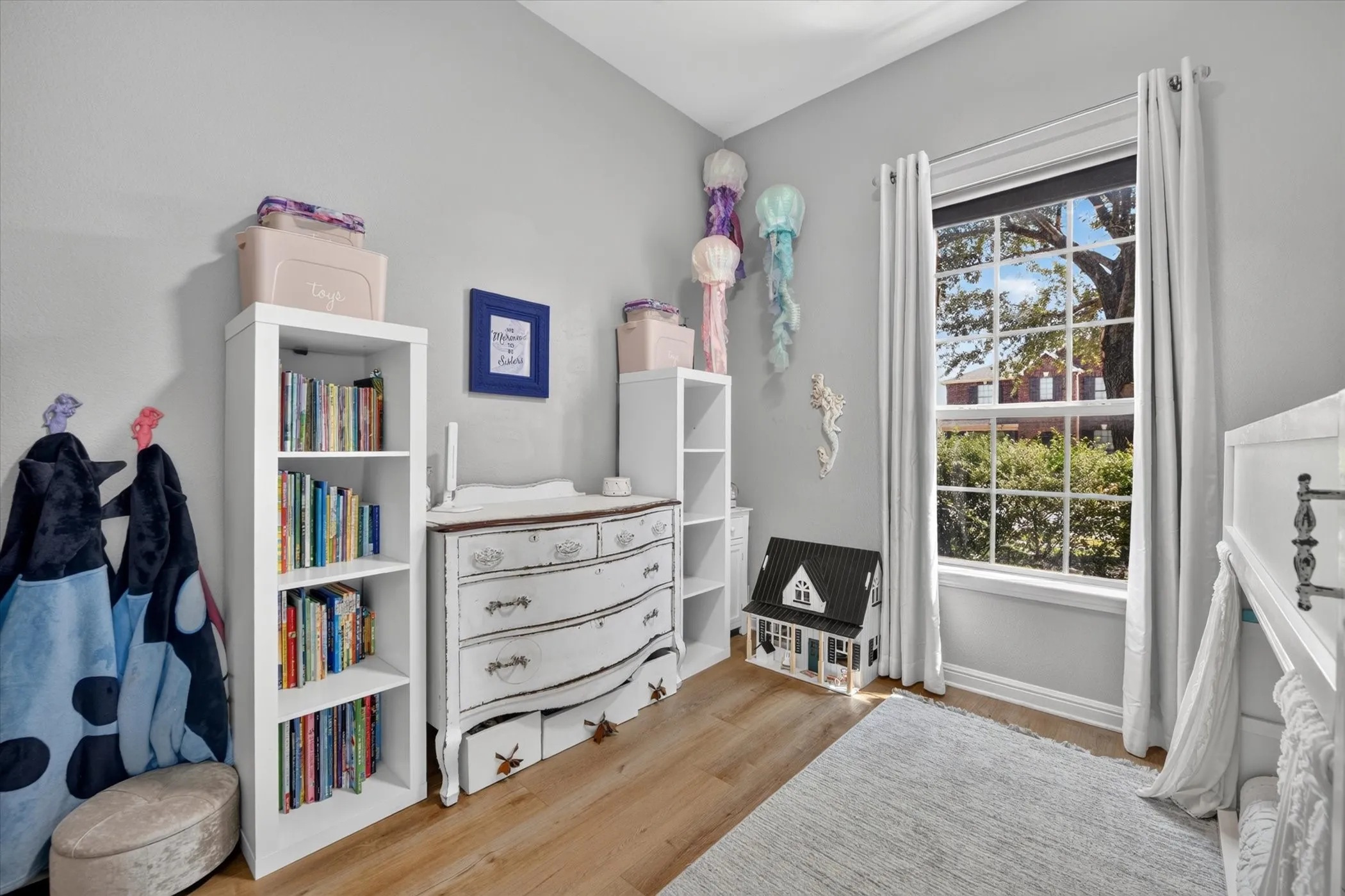 Vaulted ceiling, wood-finish flooring, white trim, large window with grid pattern, and neutral wall color