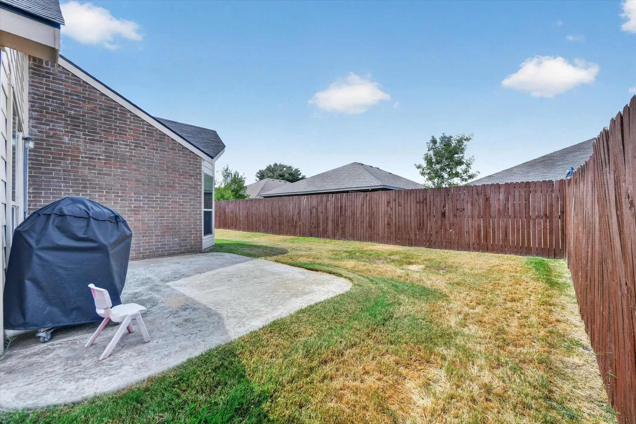 Expansive backyard featuring a privacy fence, concrete patio, and brick exterior