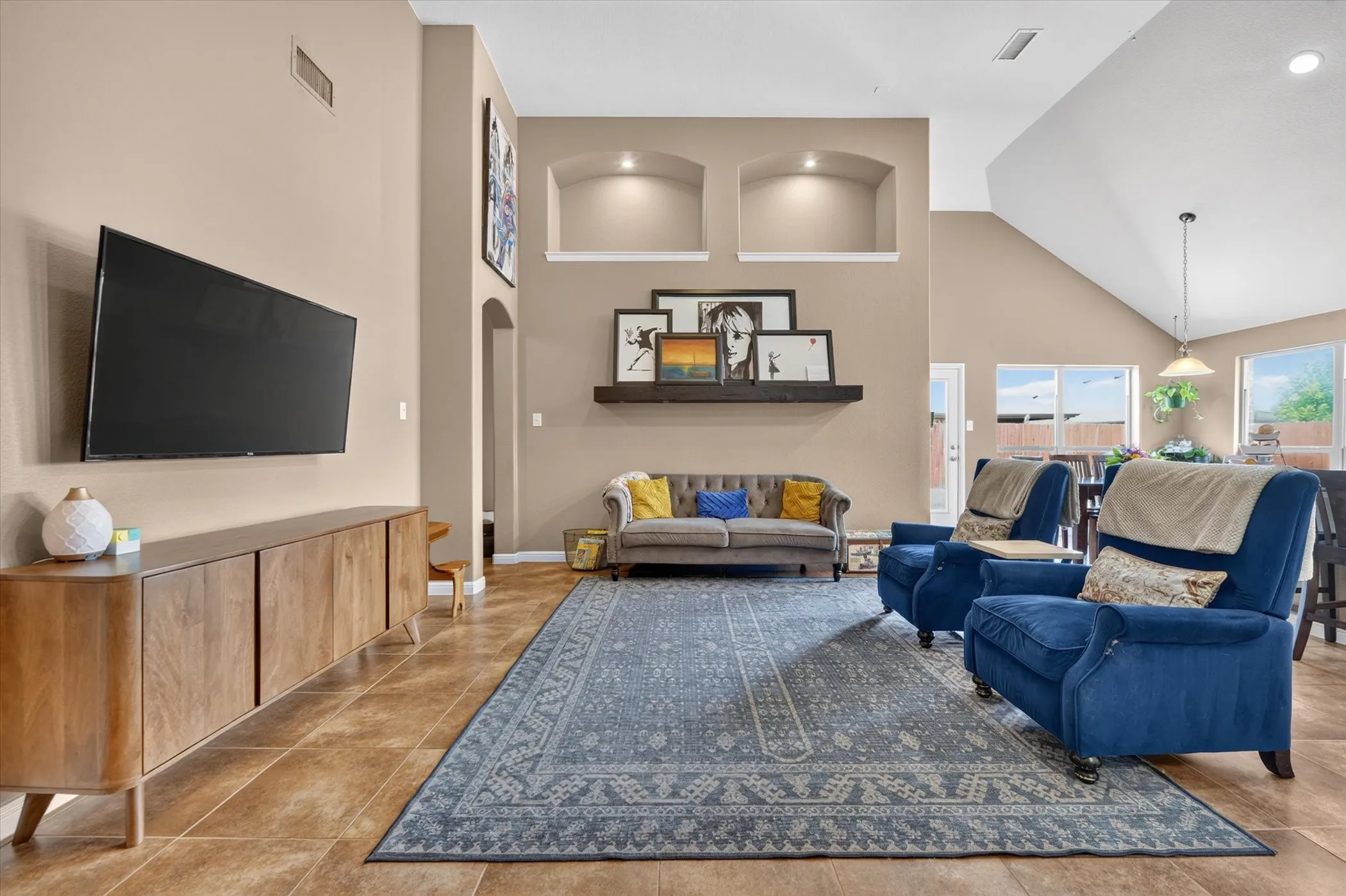 Vaulted ceiling with an exposed beam, recessed wall niches with accent lighting, tile flooring, and multiple windows