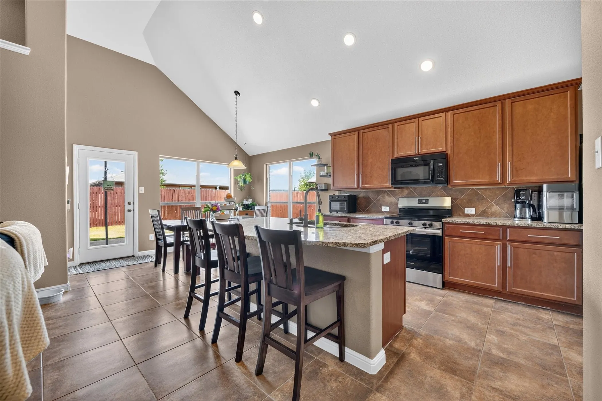 Kitchen featuring a large island, wood-finish cabinetry, tile flooring, and vaulted ceiling