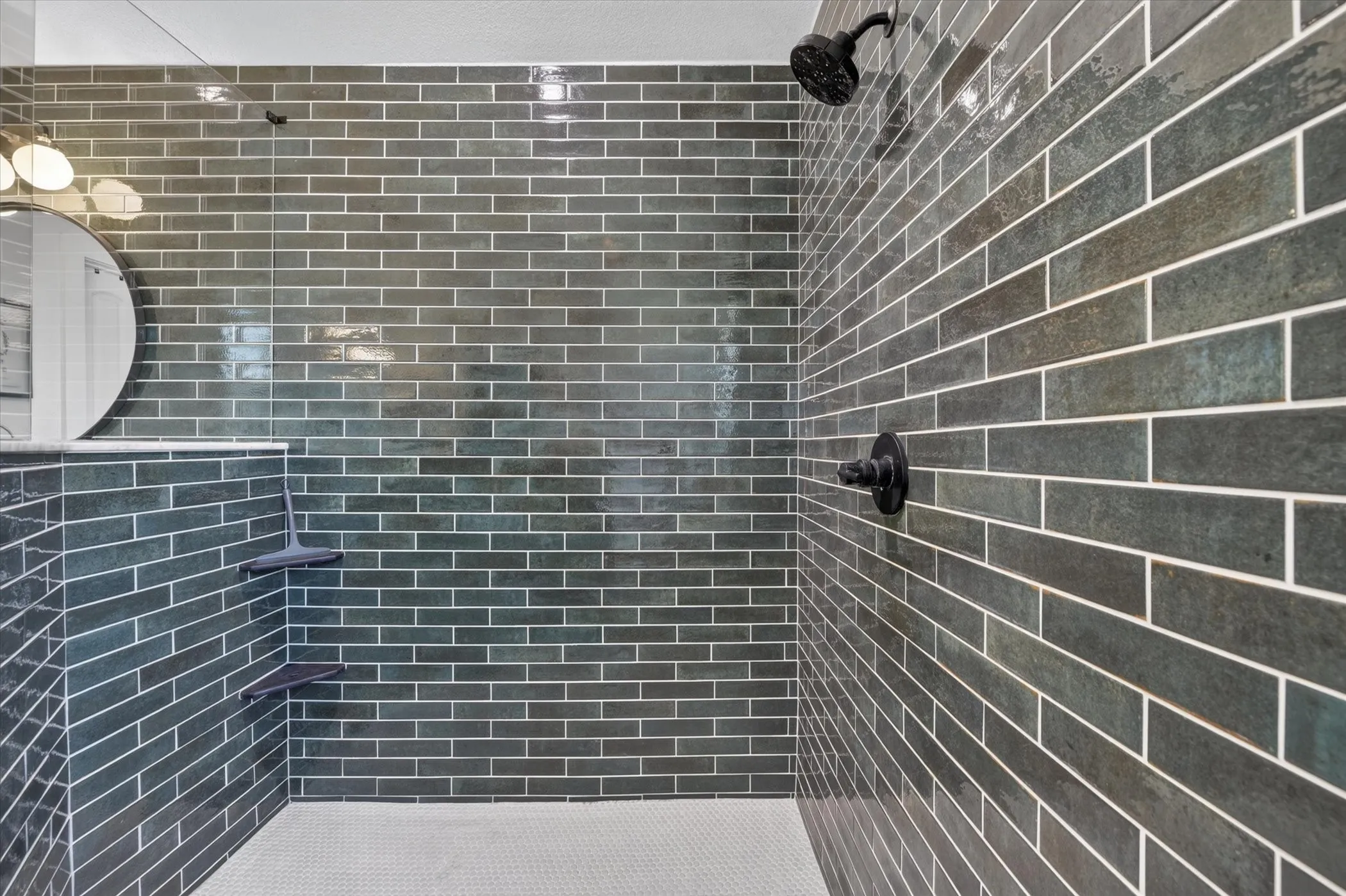 Walk-in shower with dark subway tile, integrated corner shelves, mosaic tile flooring, and matte black fixtures
