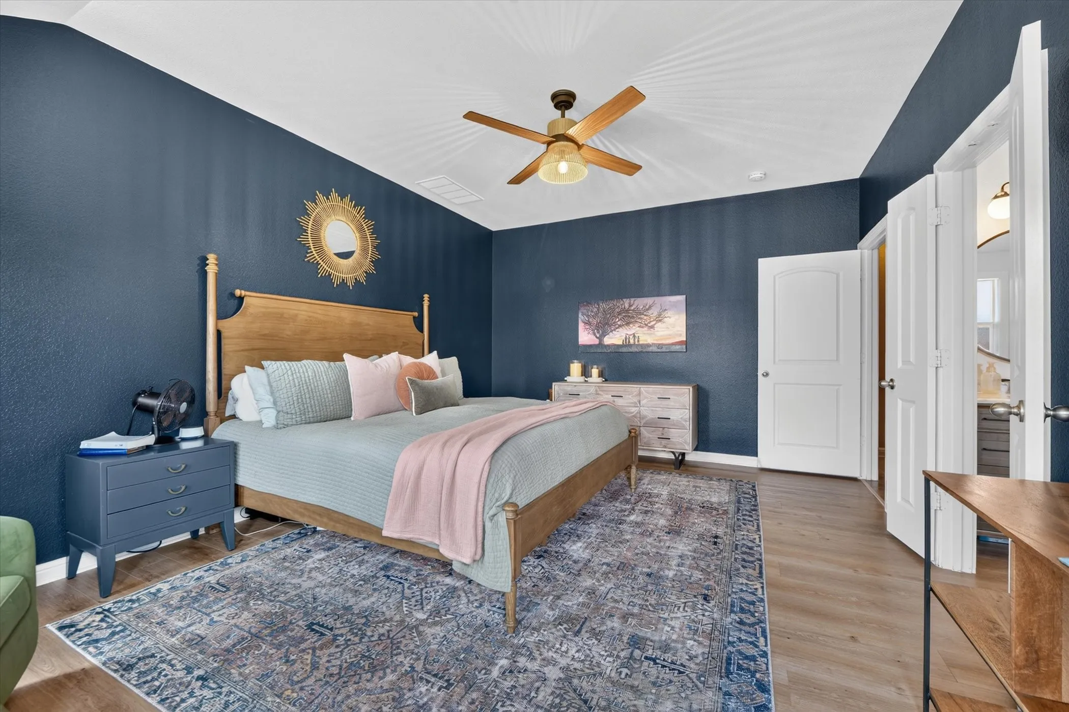 Wood-finish flooring, accent wall, ceiling fan, and white interior doors