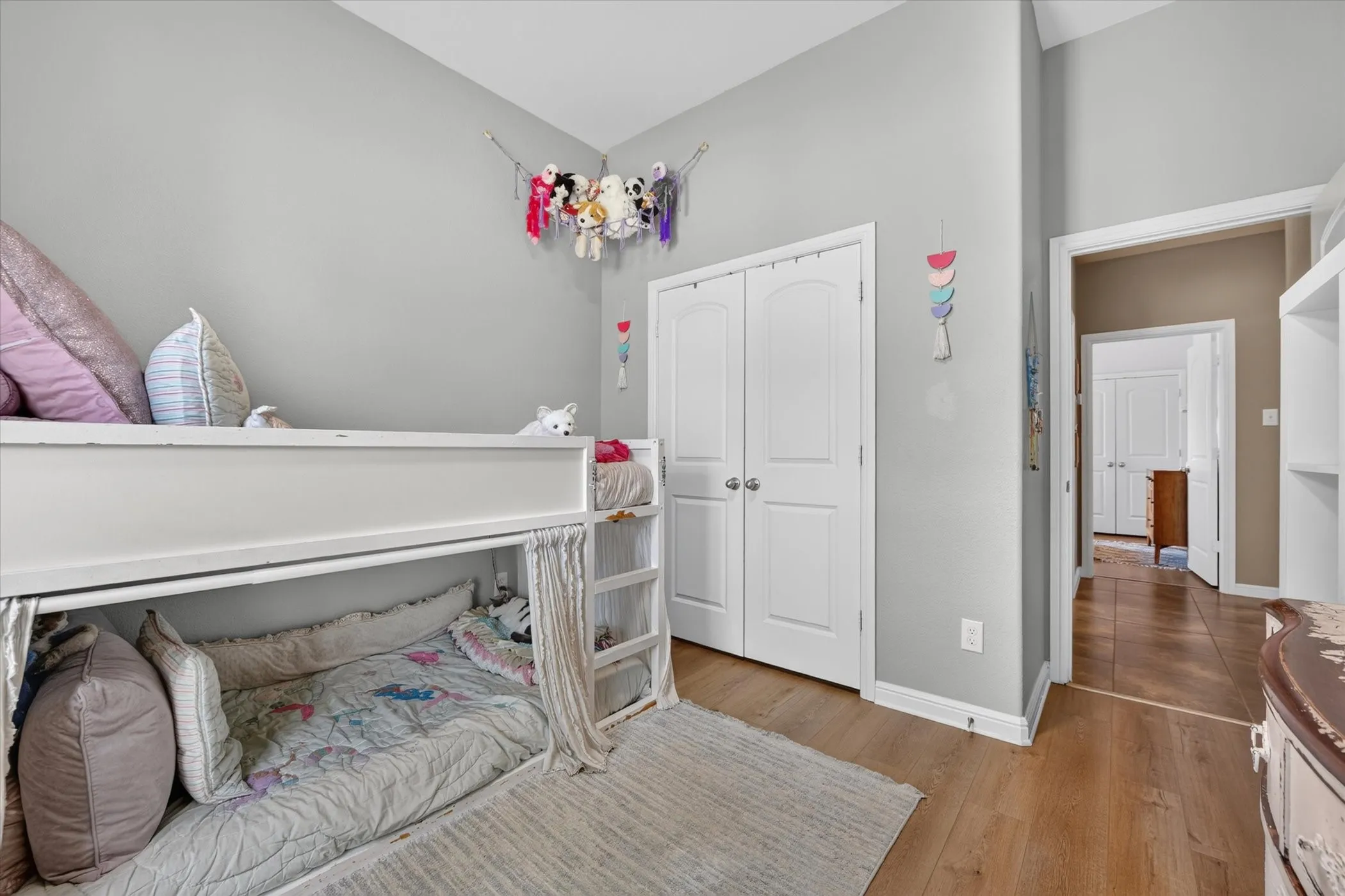 Bright bedroom featuring hardwood flooring, built-in lofted bed with storage underneath, dual closets with white six-panel doors, and soft neutral wall finishes