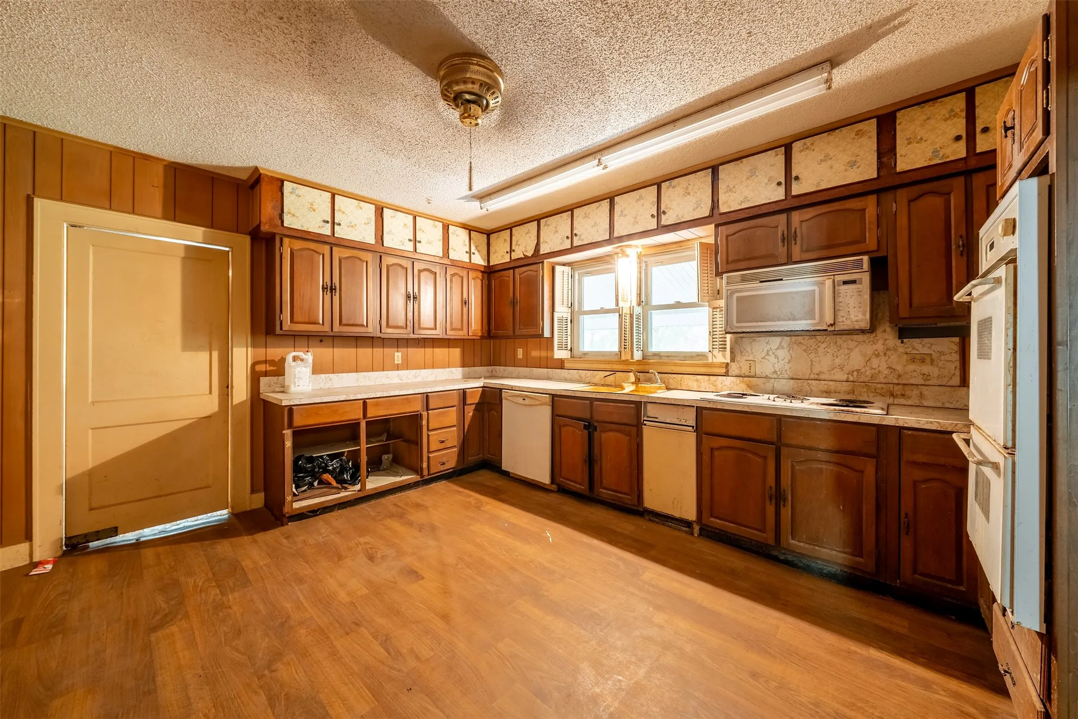 Kitchen with wood-finish flooring, wood paneling, extensive wood cabinetry, white countertops, and a double wall oven