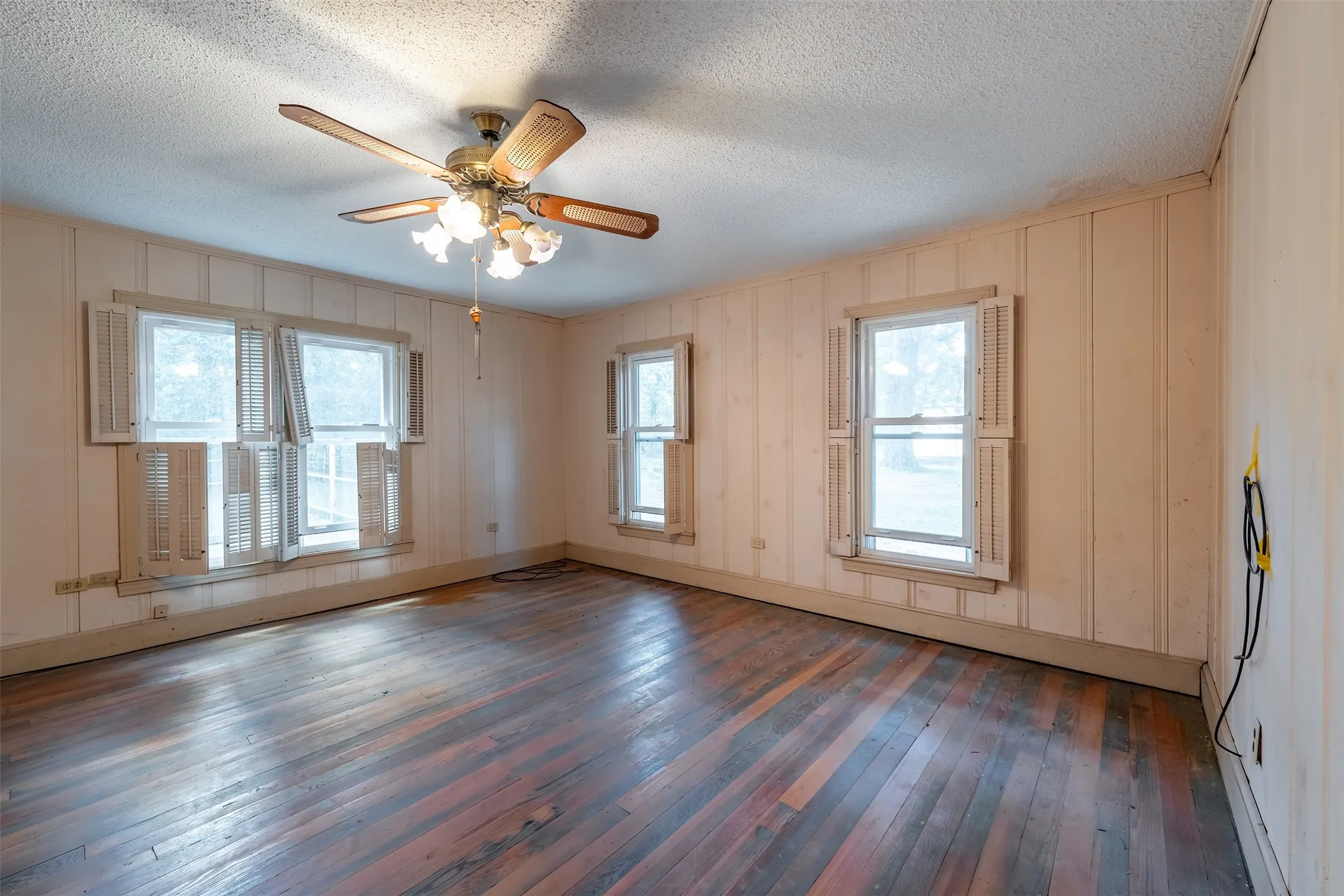 Hardwood flooring, wall paneling, ceiling fan with integrated lighting, multiple windows, window shutters