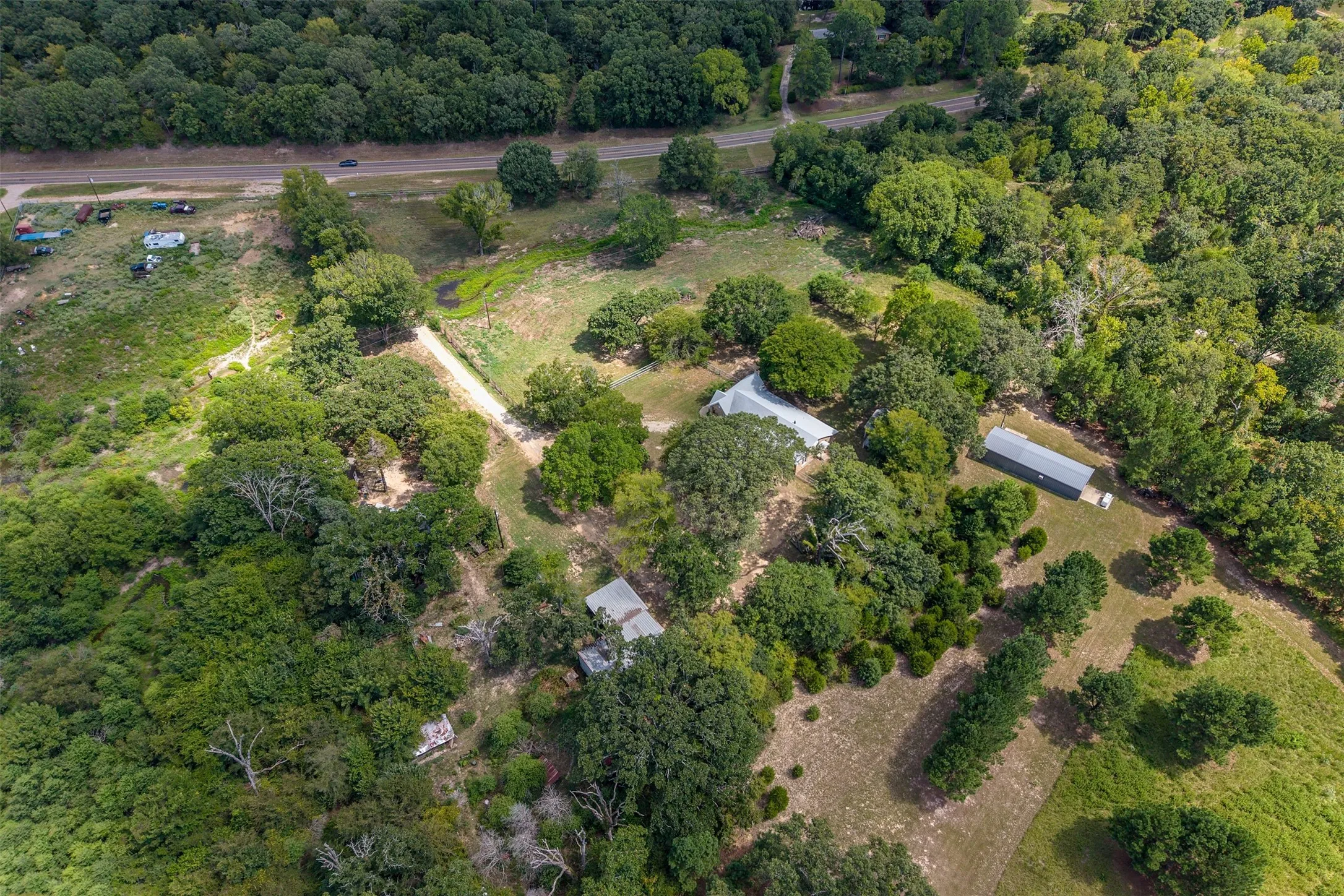 Extensive acreage with multiple structures, mature trees, and a visible roadway