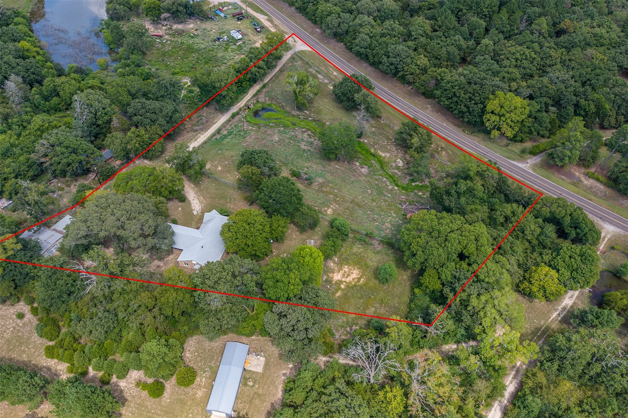 Expansive acreage featuring a main residence, a secondary structure, a pond, and dense mature trees