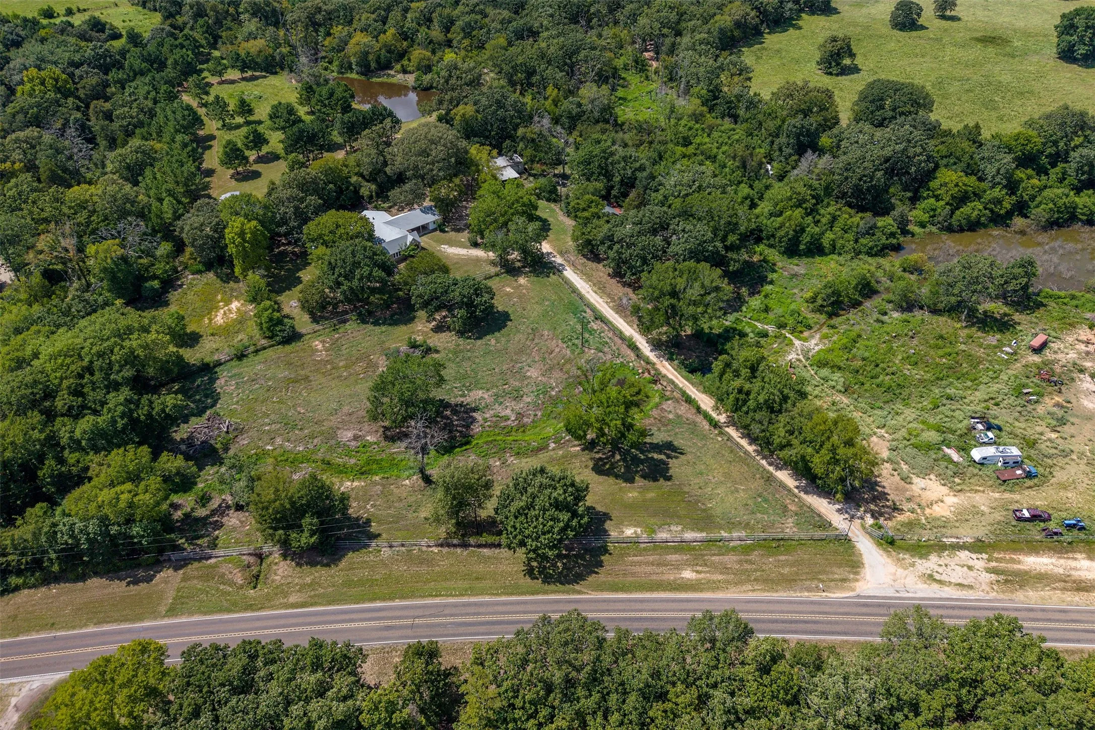 Rural property featuring extensive tree coverage, a private pond, and a gravel drive