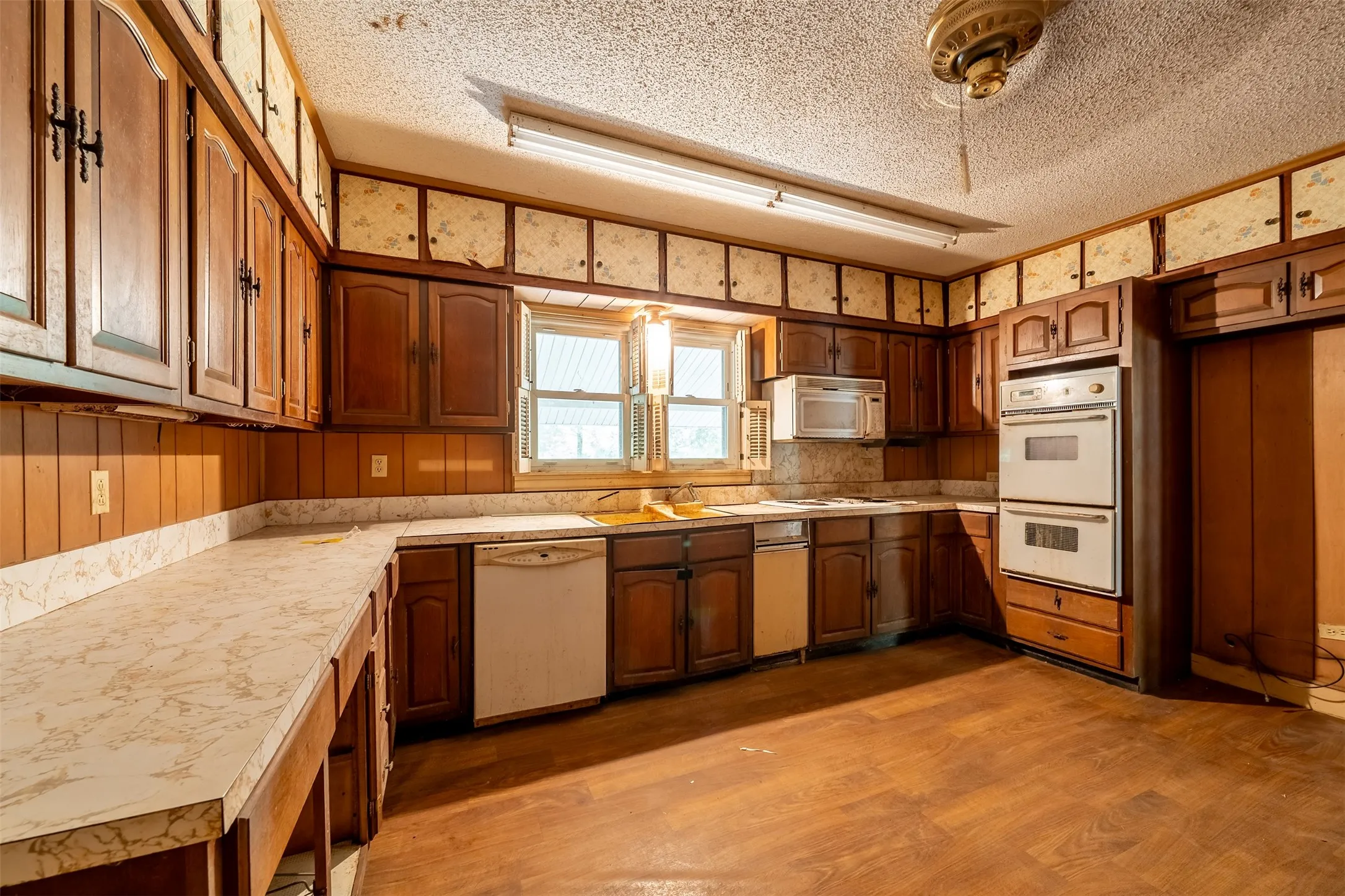 Kitchen featuring wood-finish cabinetry, built-in double ovens, and a window above the sink