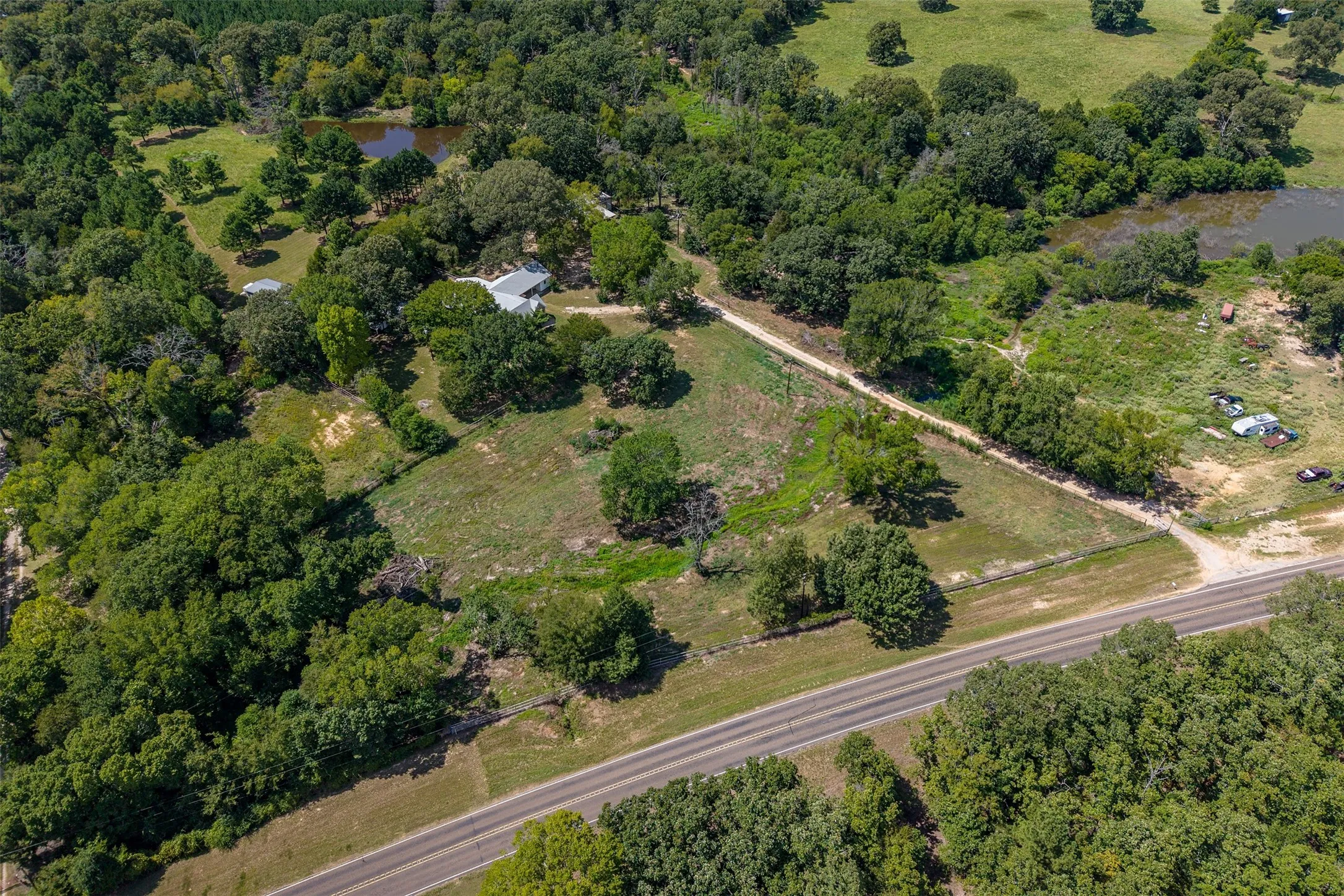 Expansive property featuring a paved road frontage, natural ponds, mature trees, and open land sections