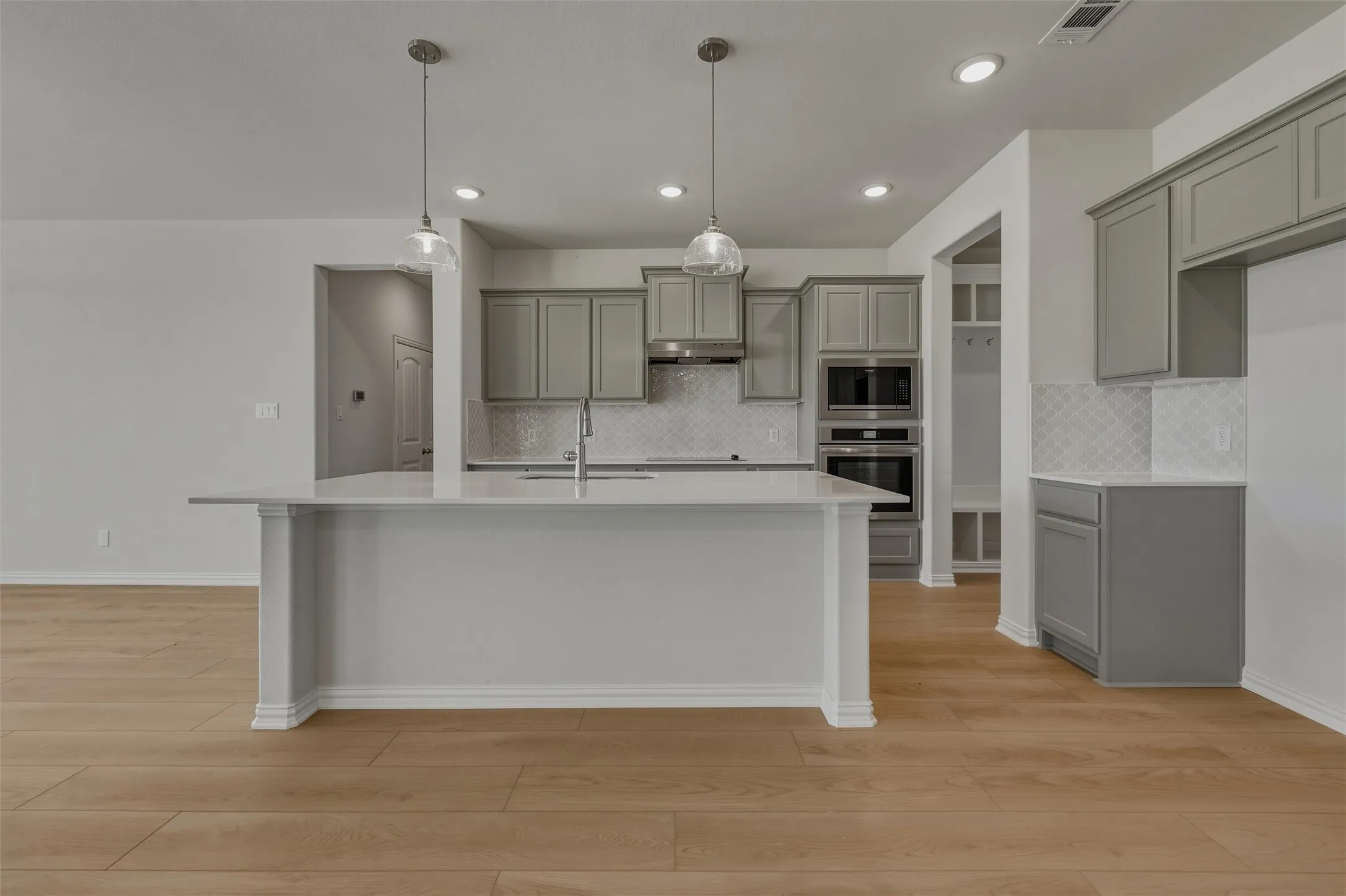 Kitchen featuring an island with countertop seating, wood-finish flooring, recessed lighting, pendant lighting, and built-in double ovens