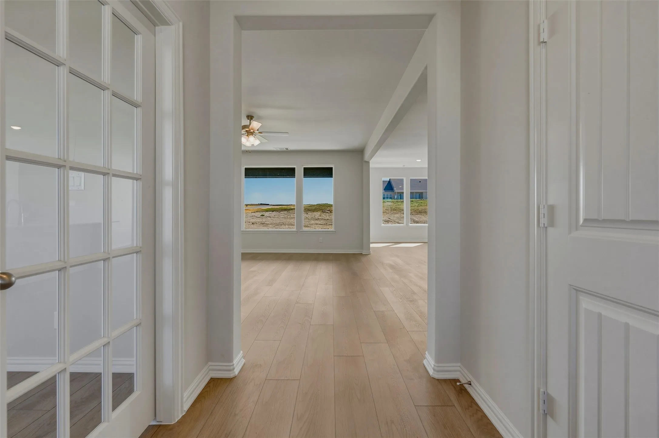 Wood-finish flooring throughout, French doors with glass panes, white paneled interior door, open archway, and white trim