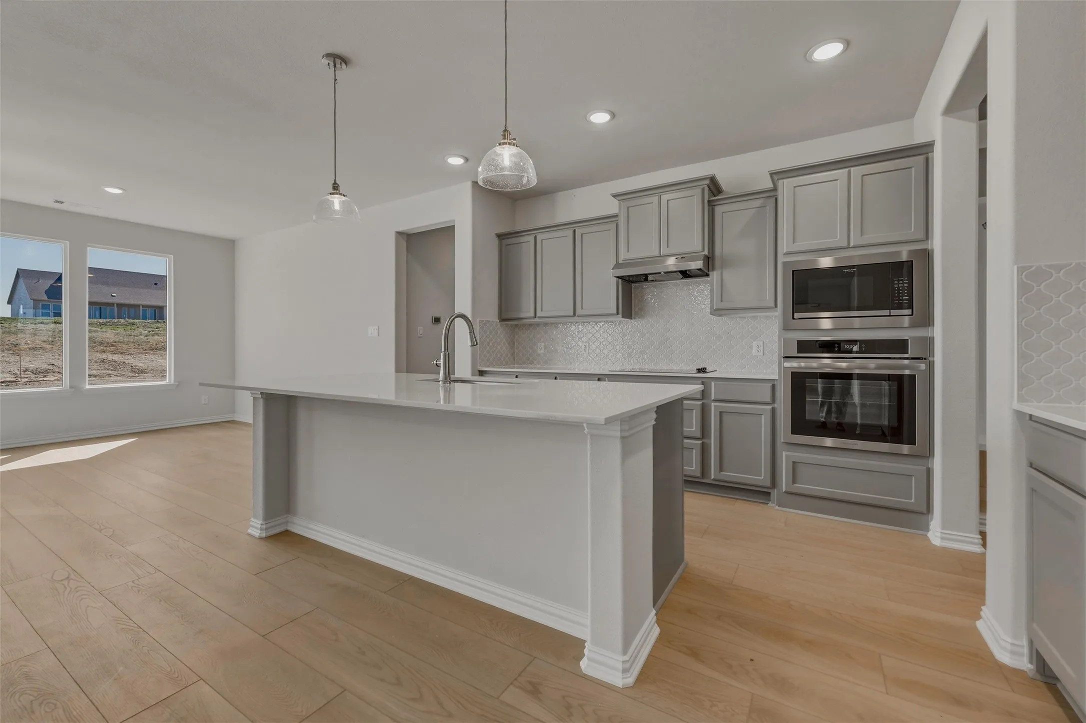 Gourmet kitchen featuring a large central island, stainless steel built-in appliances, custom cabinetry, tiled backsplash, and wood-finish flooring