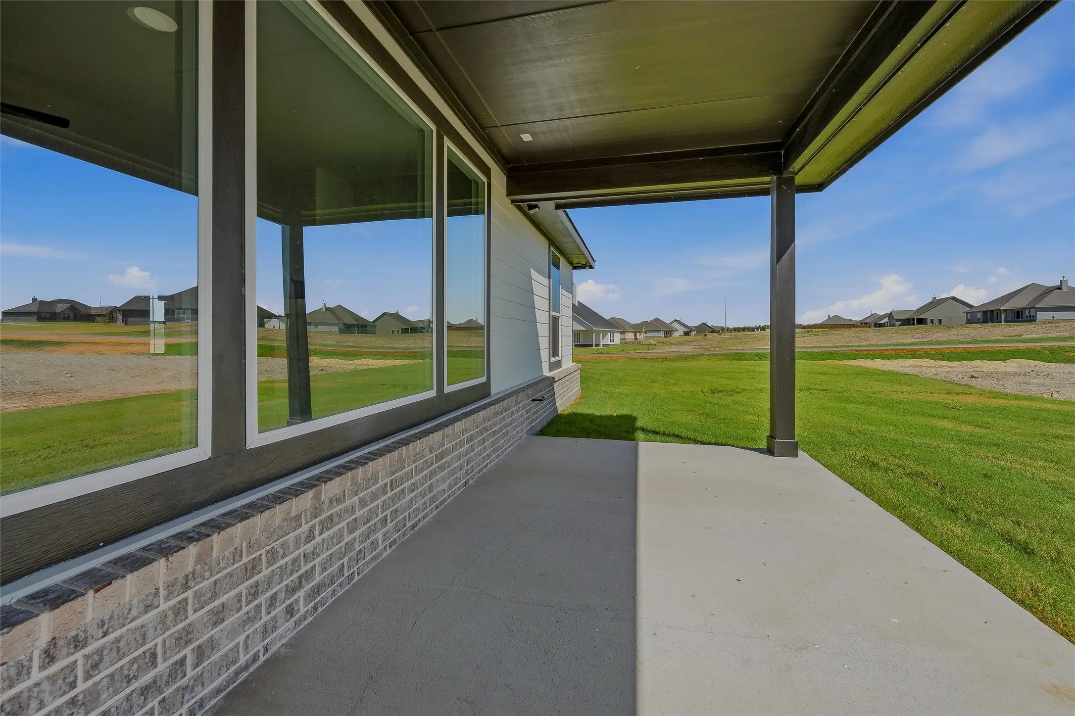 Covered patio with concrete flooring, brick exterior siding, and a large window wall