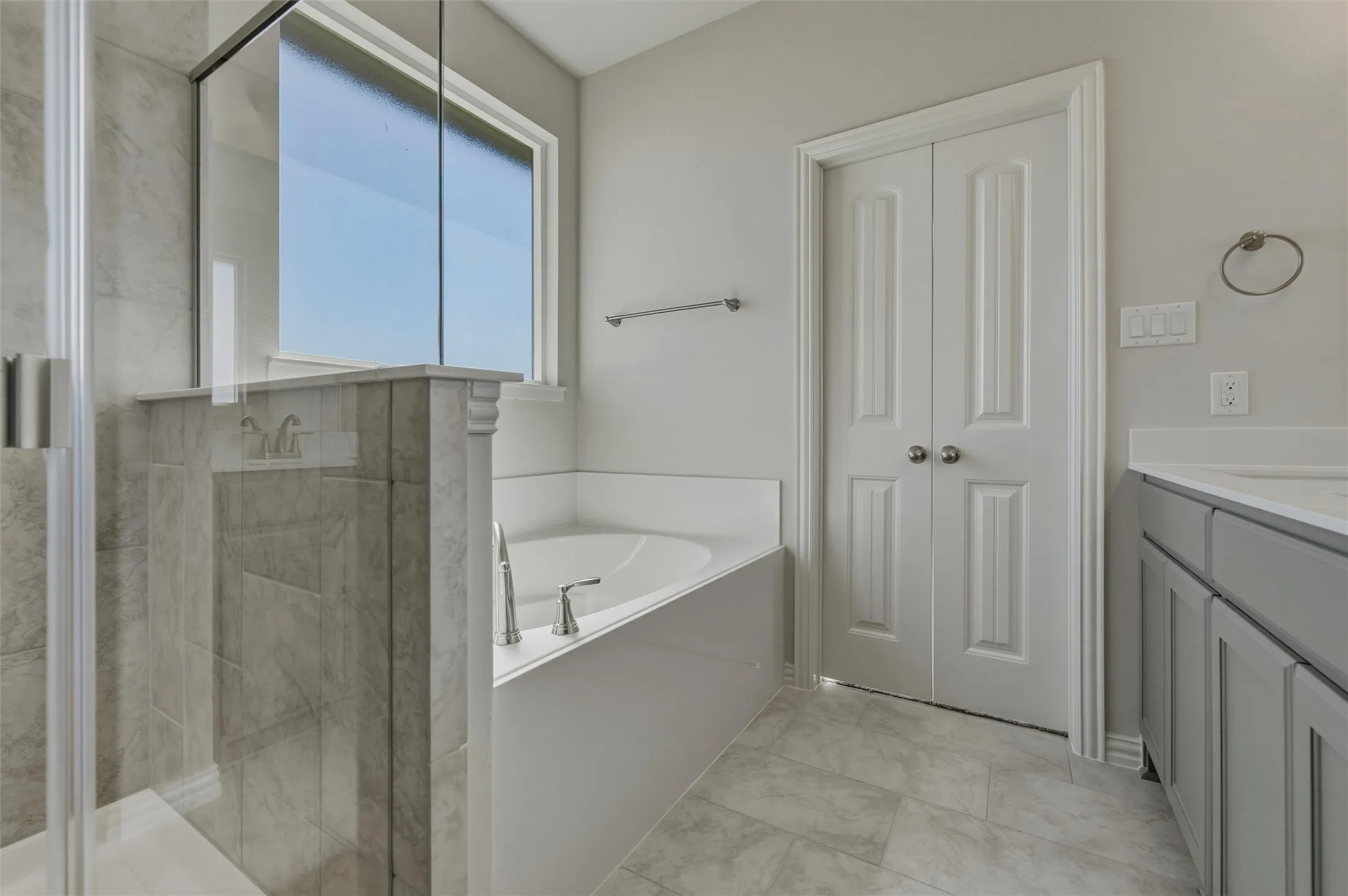 Spacious bathroom featuring a built-in soaking tub, a separate glass-enclosed shower, dual vanity with undermount sinks, and light gray cabinetry