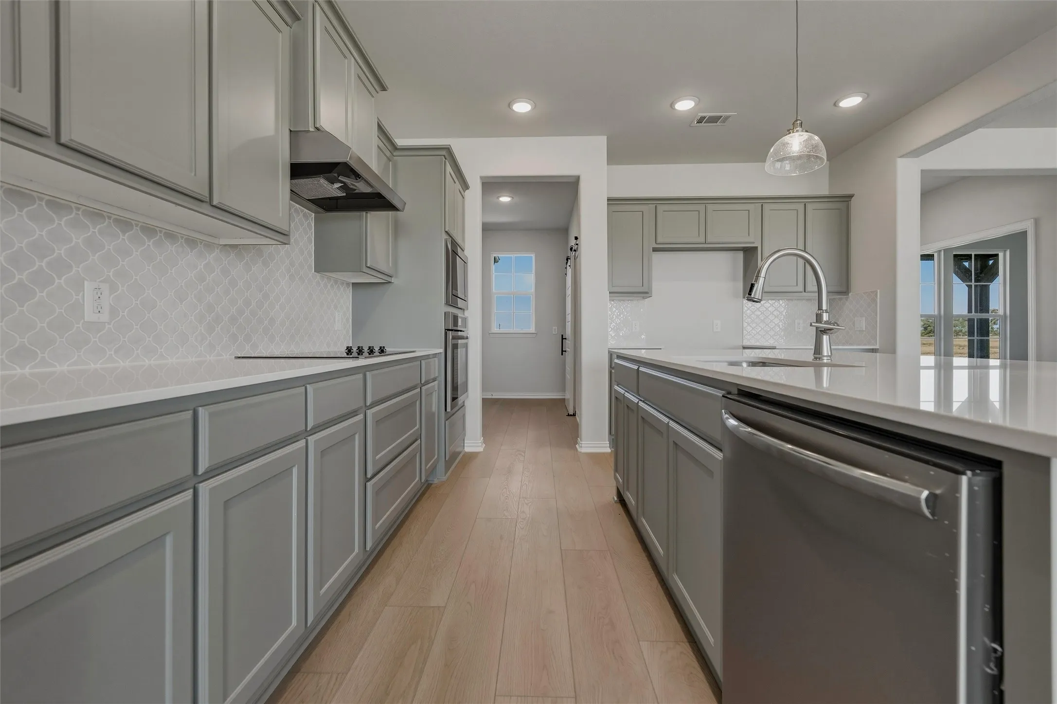 Kitchen featuring gray cabinetry, light wood-finish flooring, stainless steel appliances, a tile backsplash, and recessed lighting