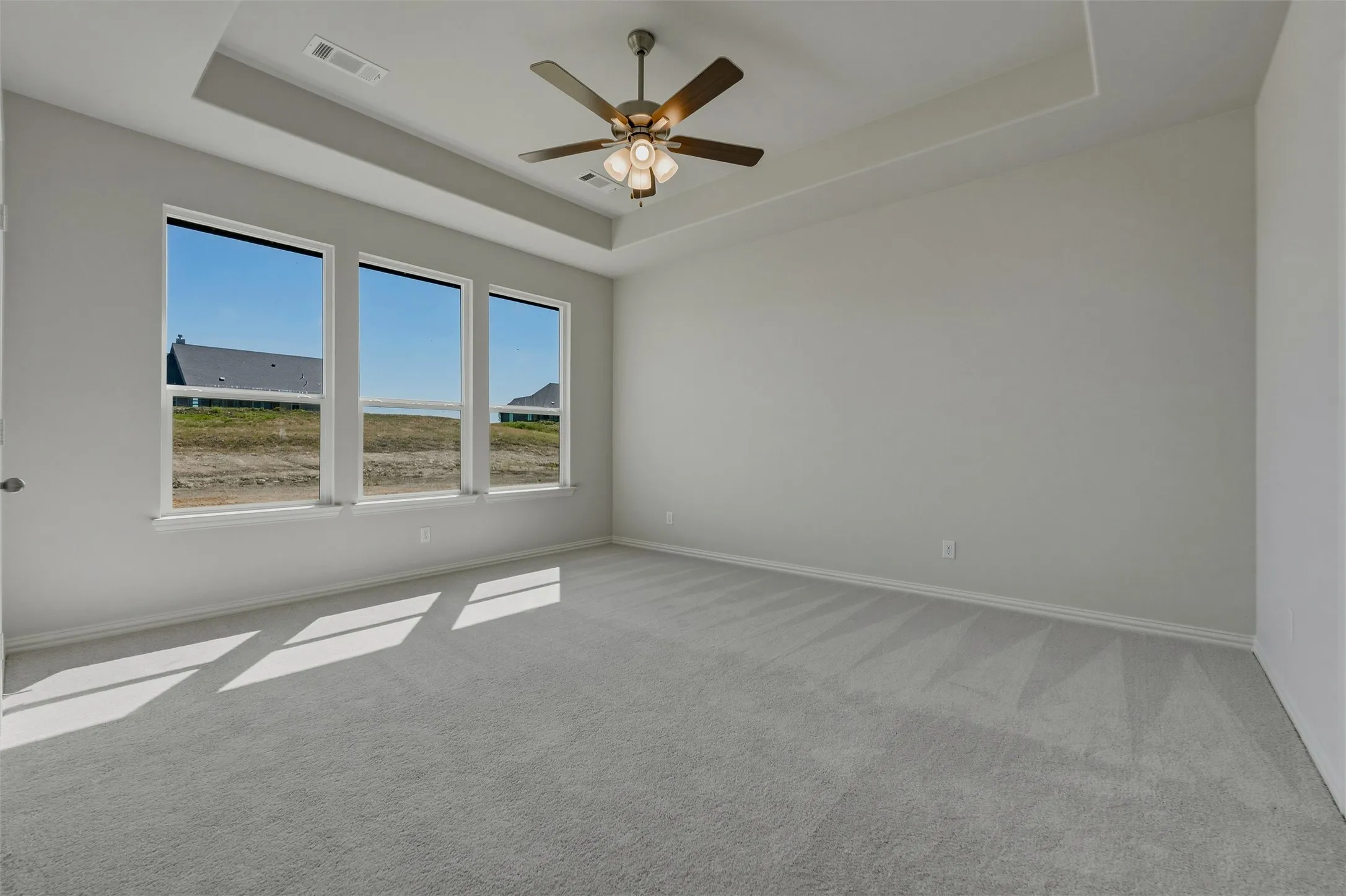 Tray ceiling with a ceiling fan, three paneled windows, and gray wall-to-wall carpeting