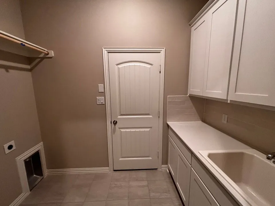 Built-in utility sink, white shaker cabinetry, light-toned countertop, and tiled flooring