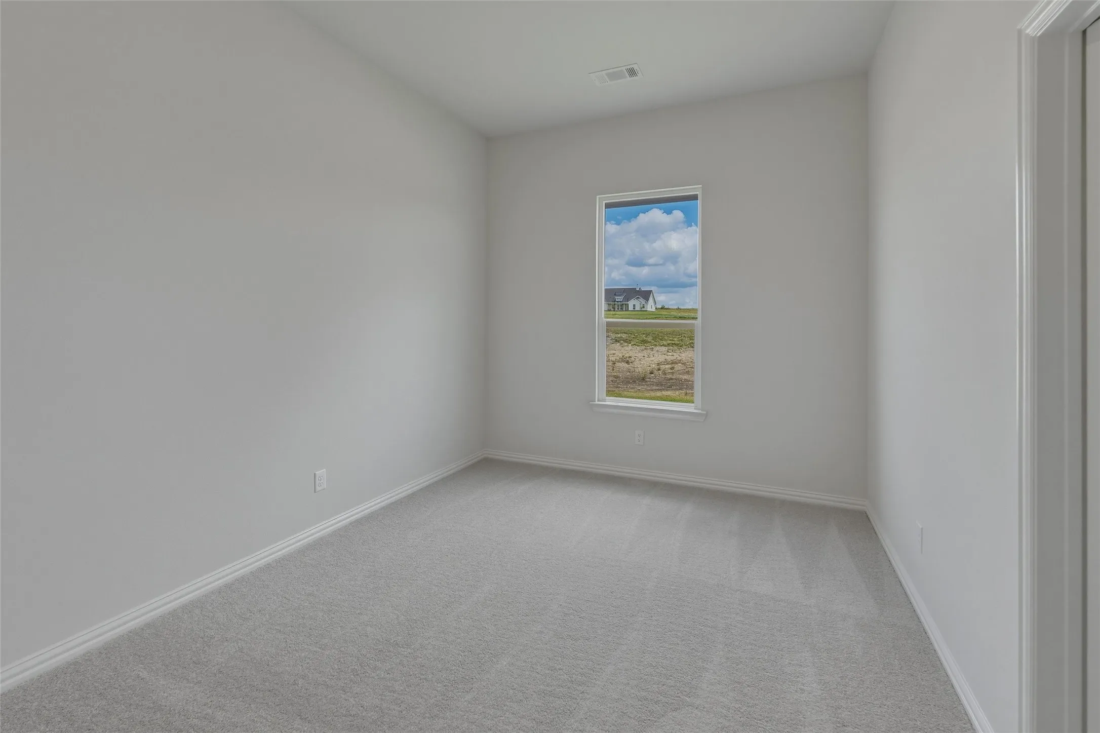 Bright, light-filled bedroom with neutral wall finishes, plush carpeting, and a large window framing pastoral scenery