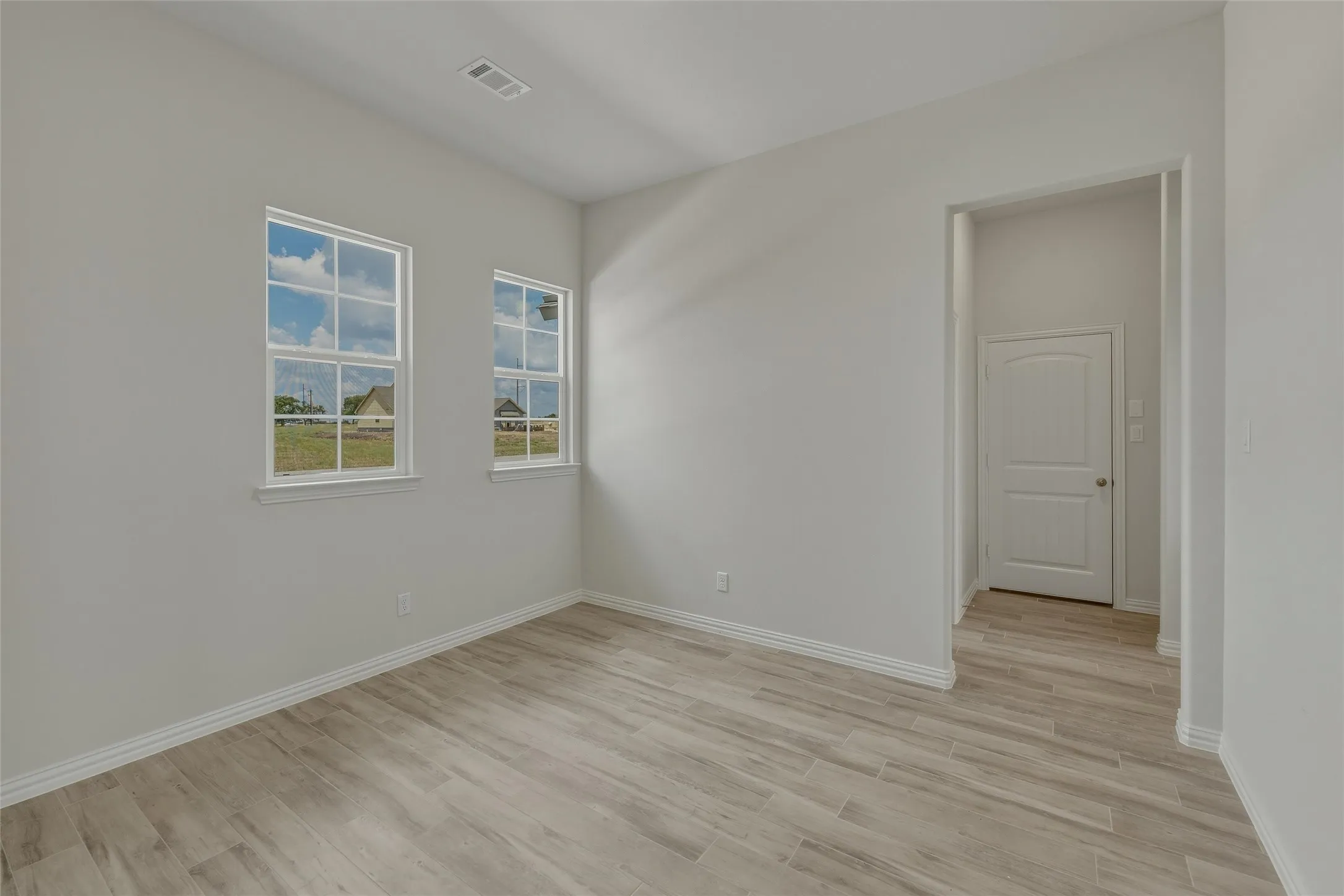 Light wood-finish flooring, white trim, two clear pane windows, recessed lighting, and a white two-panel interior door