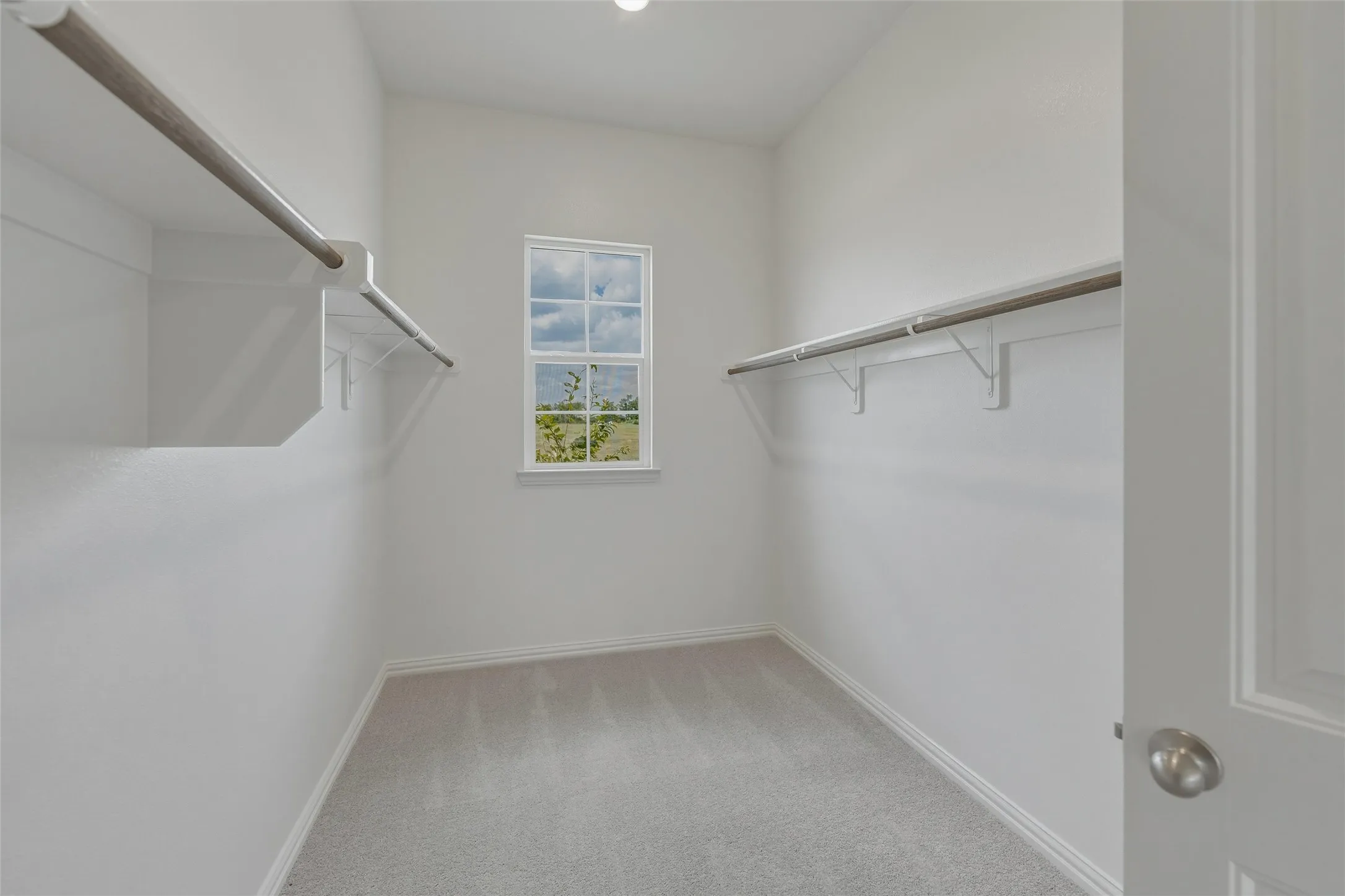 Recessed lighting, window with exterior scenery, overhead shelving, clothes rods, and light gray carpeting