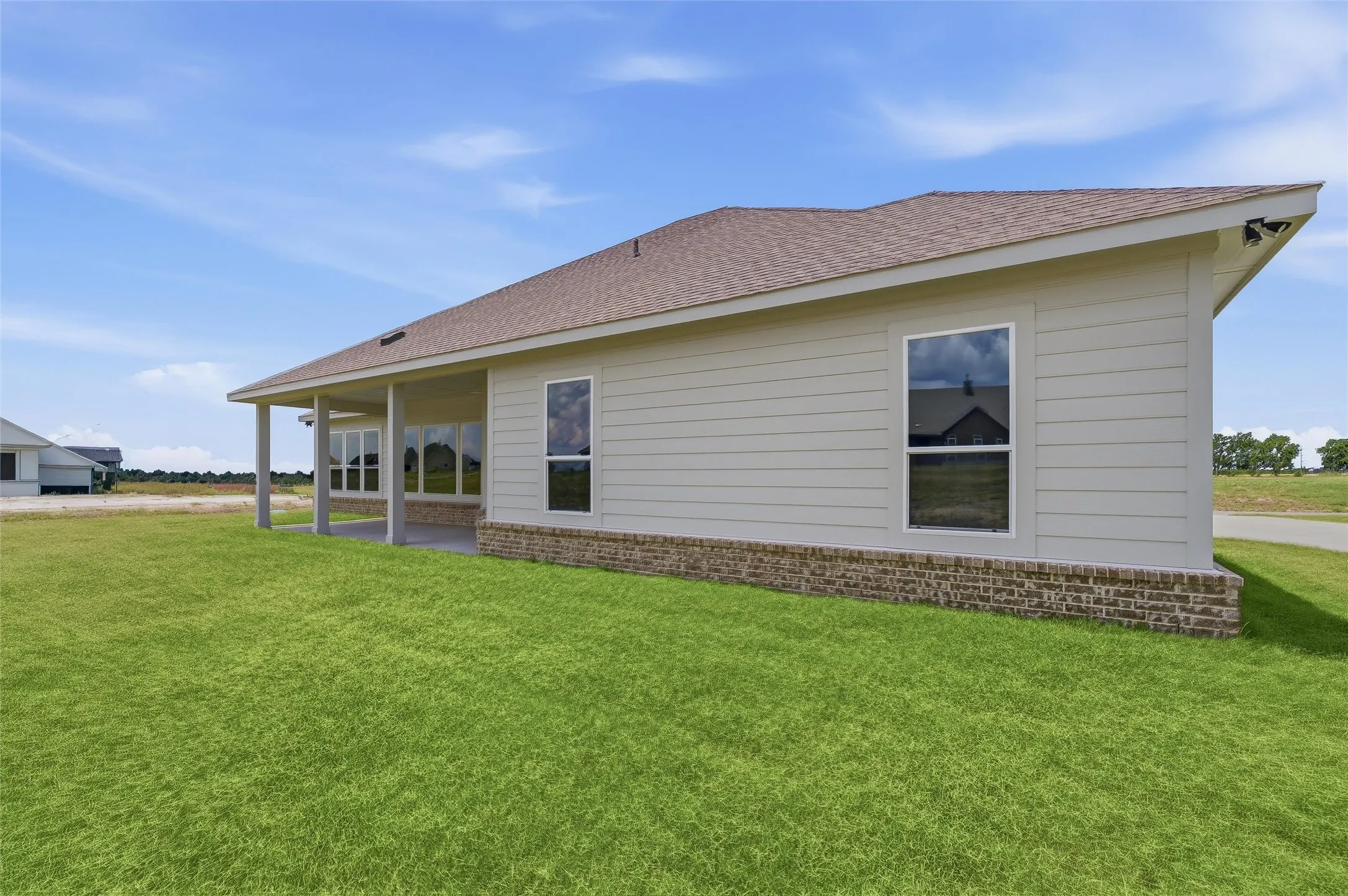 Expansive green lawn, covered patio, brick foundation detail, horizontal siding, and multiple windows