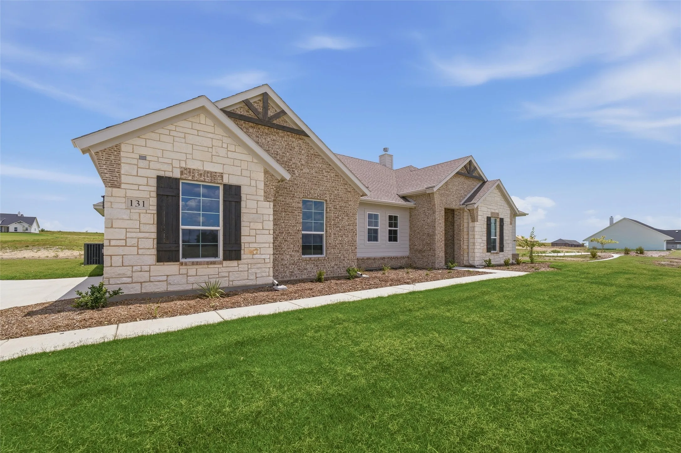 Stone and brick exterior with dark window shutters, gabled rooflines, and a concrete walkway