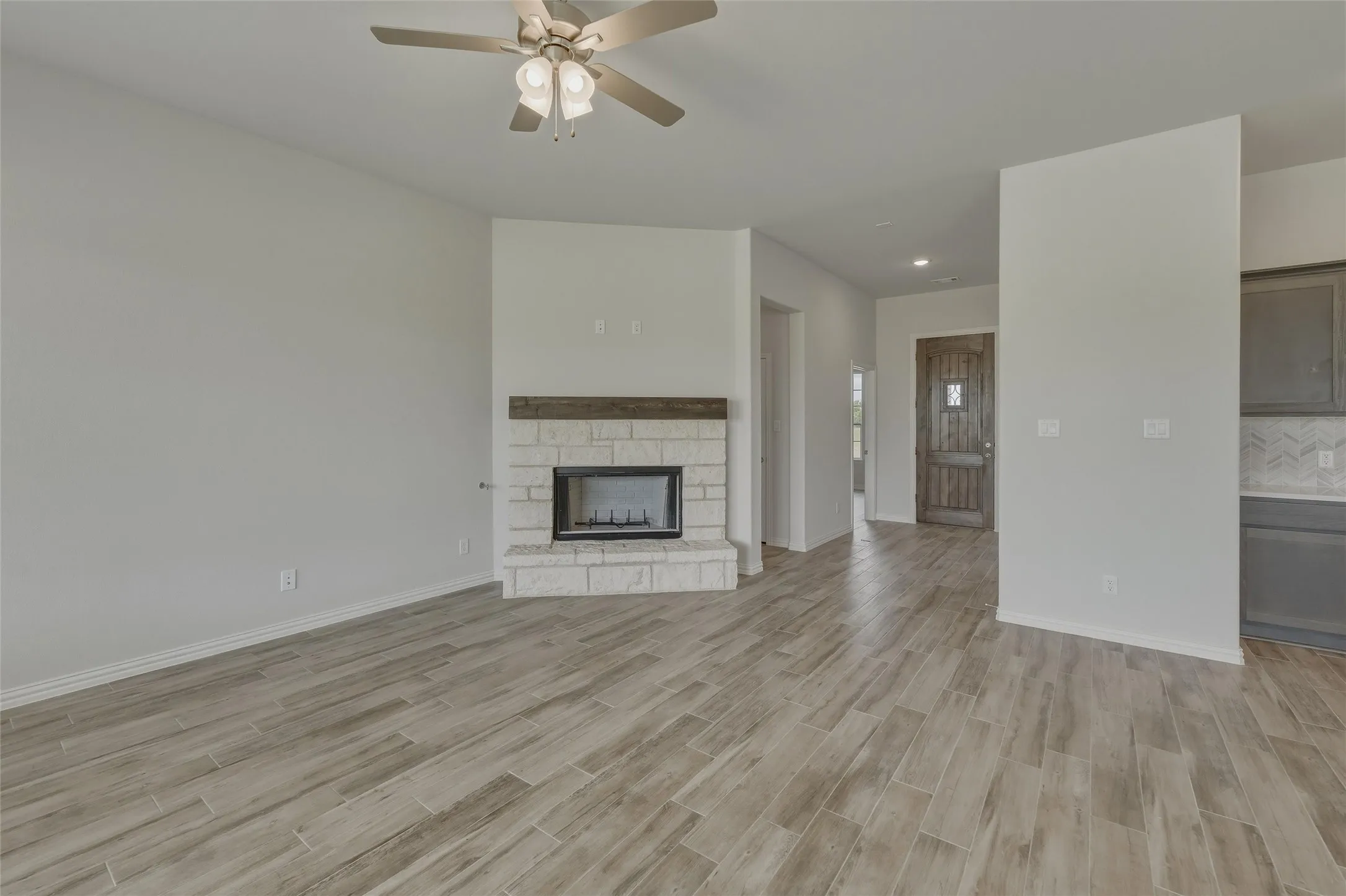 Living area featuring wood-finish flooring, a ceiling fan, a fireplace with stone surround and wood mantel, and a dark wood entry door