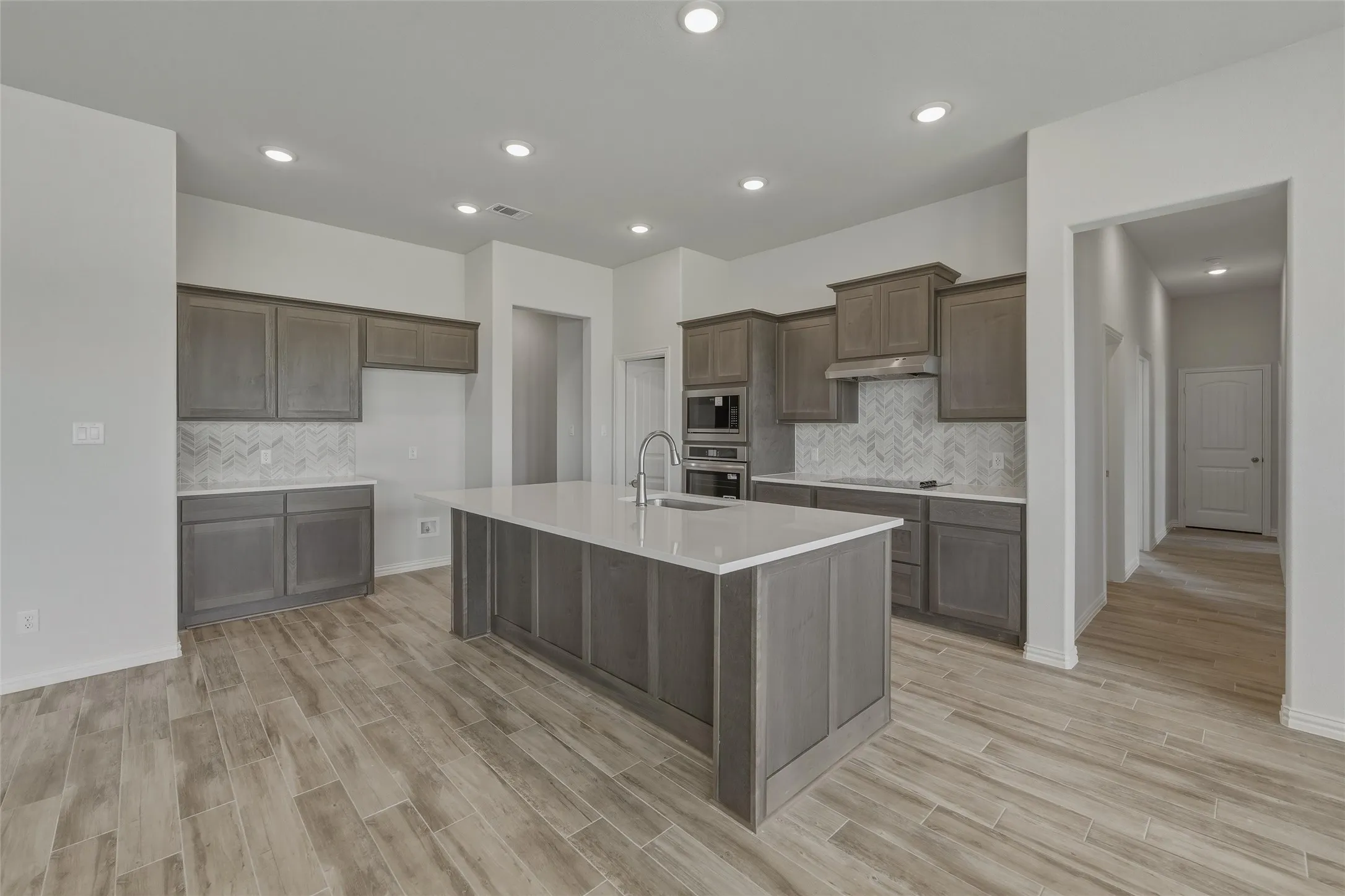 Kitchen featuring a central island, wood-finish flooring, recessed lighting, gray cabinetry, and a herringbone tile backsplash