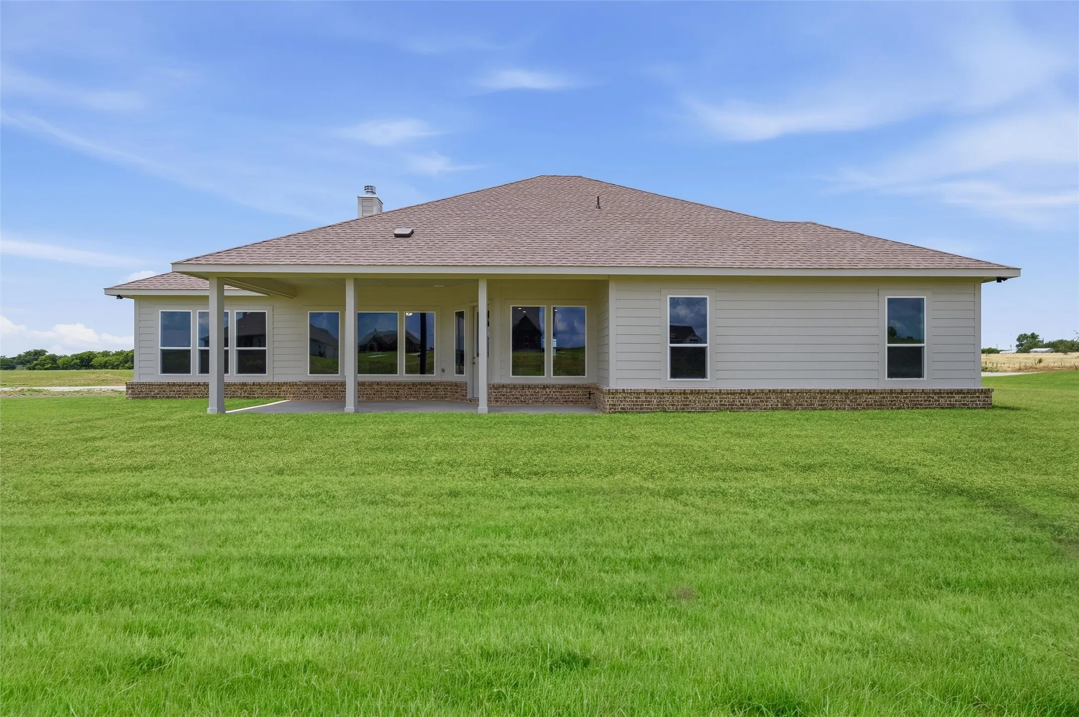 Expansive green lawn with a covered patio featuring support columns, an asphalt shingle roof, horizontal siding, and stone accents