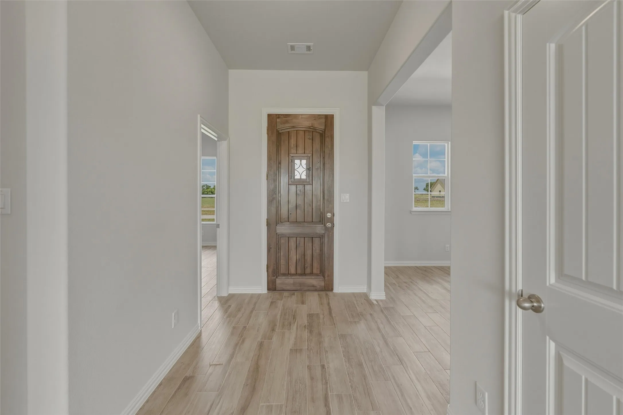 Wood-finish flooring, paneled interior door with a brushed nickel knob, recessed lighting, and a front entry door with a decorative glass insert