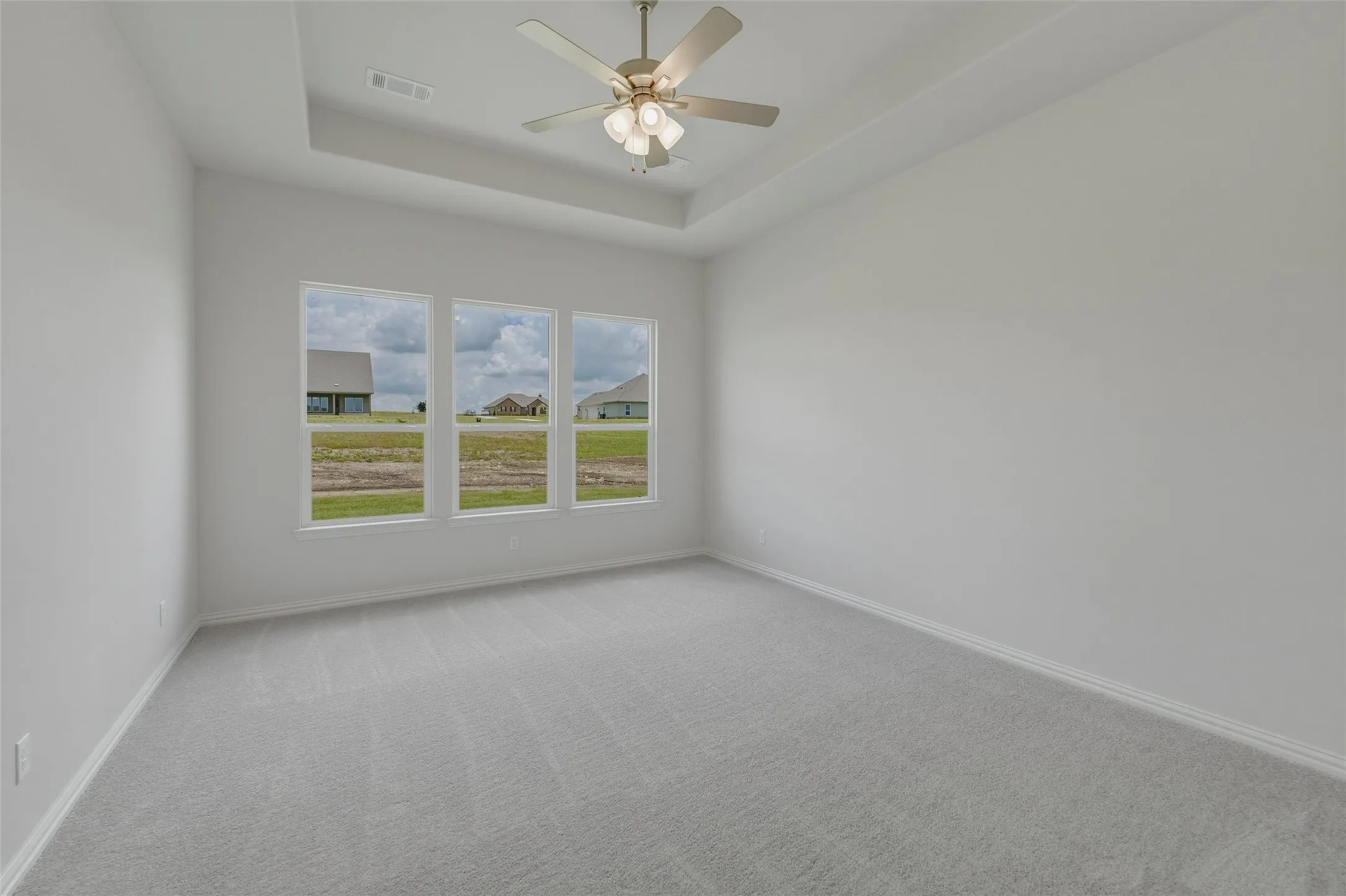 Tray ceiling with a ceiling fan light fixture, carpet flooring, and three large windows