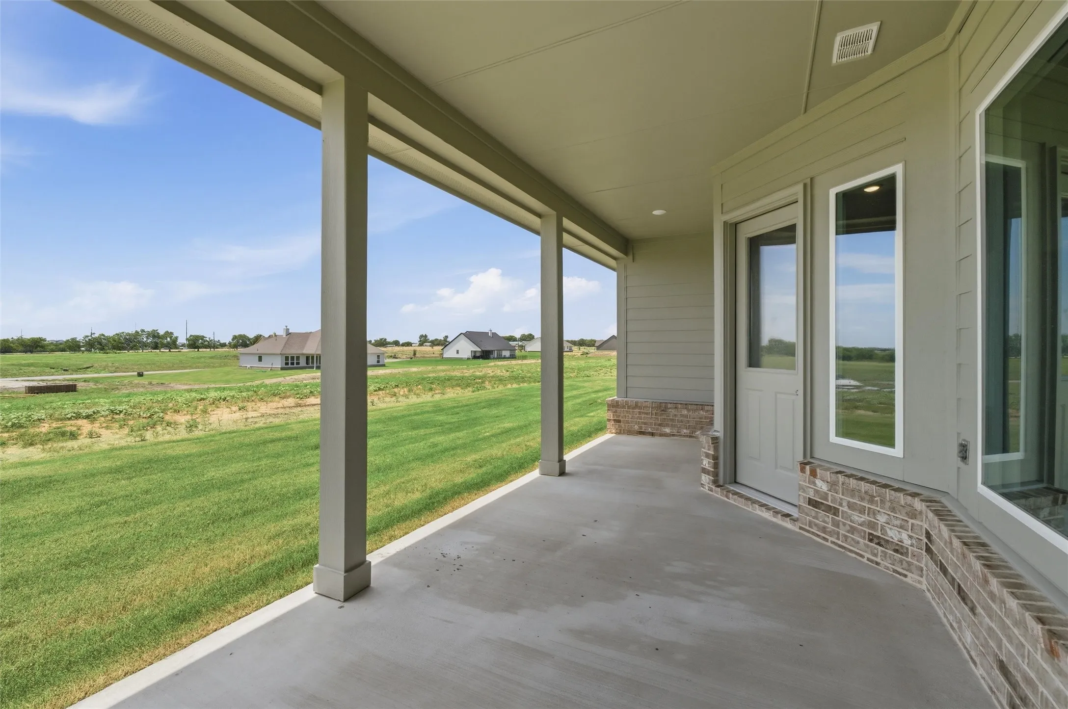 Covered concrete patio with recessed lighting, brick accents, and direct access to interior via a glass-paneled door