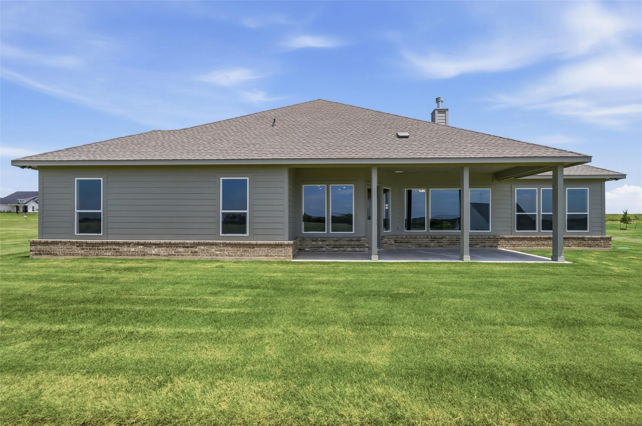 Expansive rear exterior featuring a covered patio, multiple large windows, and a brick foundation