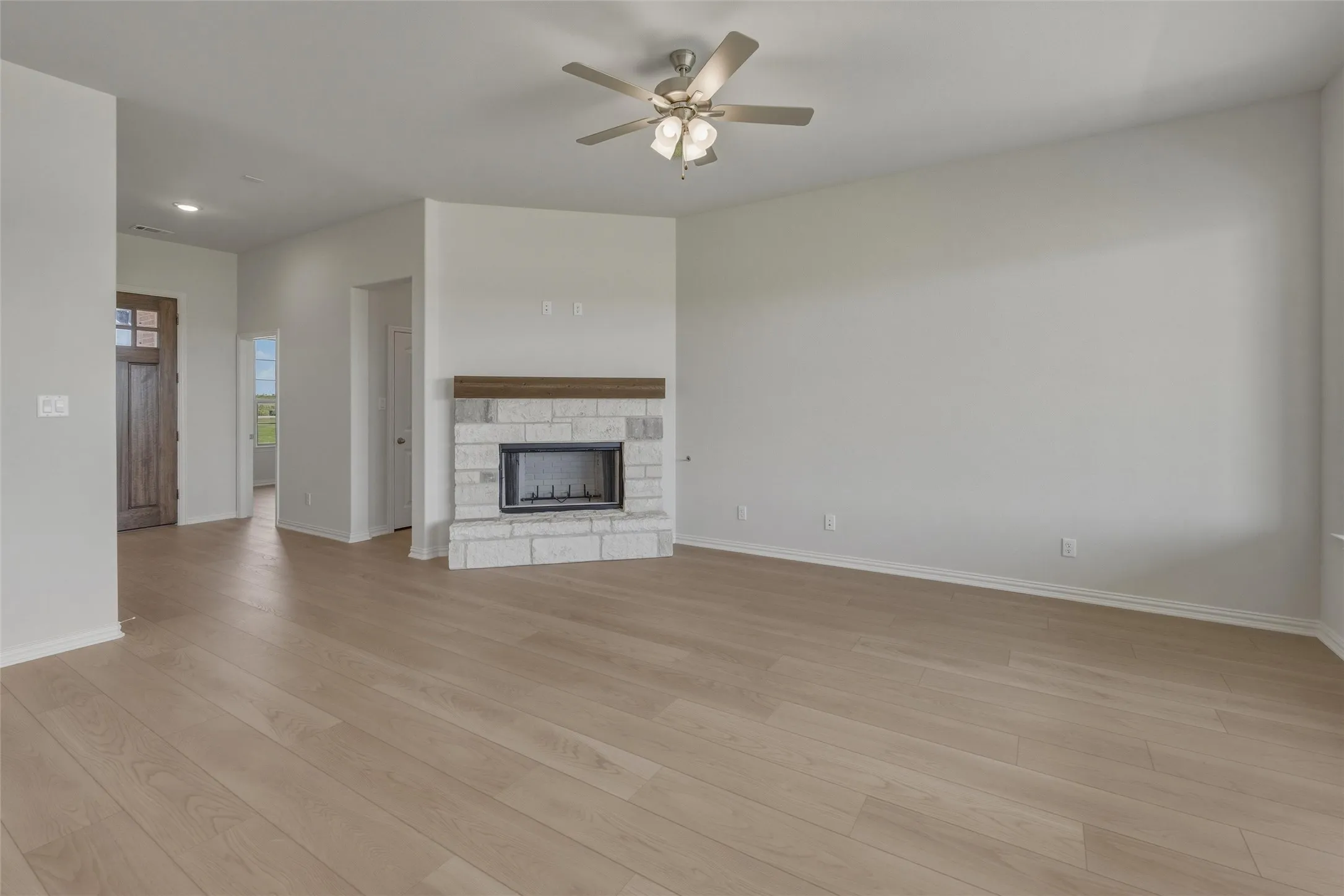 Spacious living area featuring wood-finish flooring, a stone-surround fireplace with wood mantel, and a ceiling fan