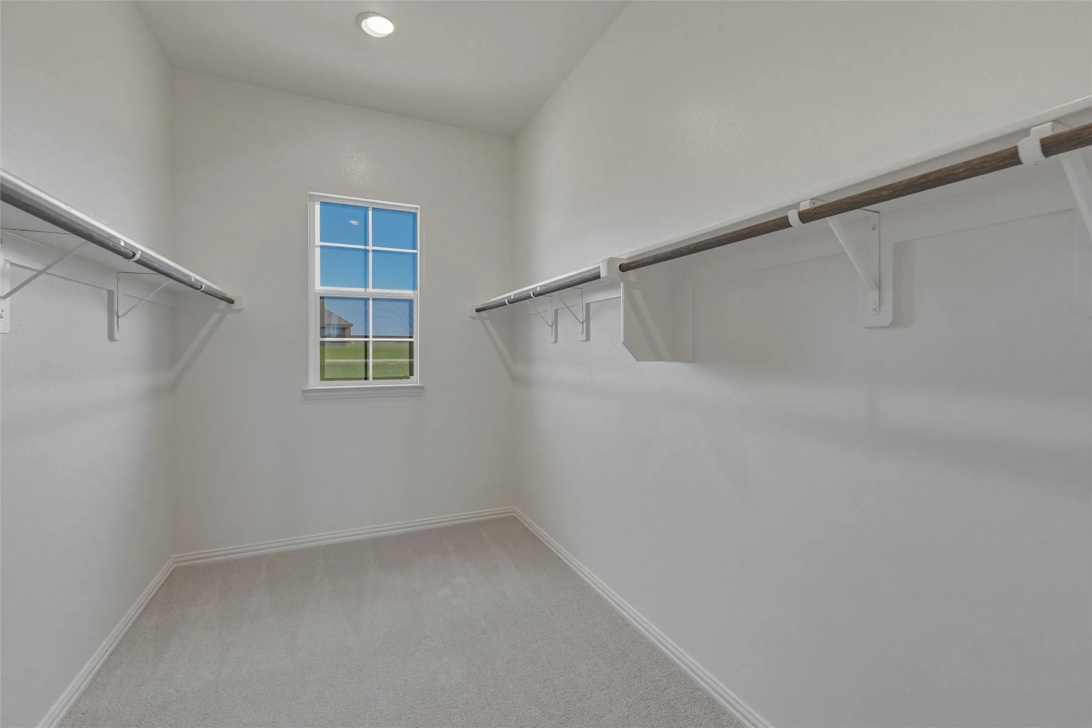 Recessed lighting, light gray carpeting, window with gridded panes, two hanging rods, and built-in shelving