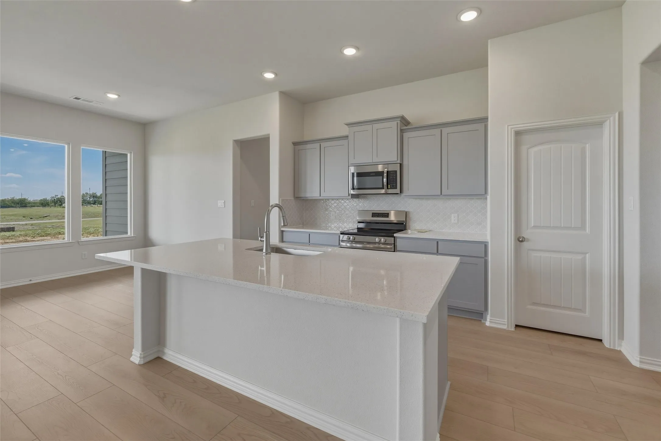 Kitchen with a large central island, light wood-finish flooring, recessed lighting, and grey cabinetry