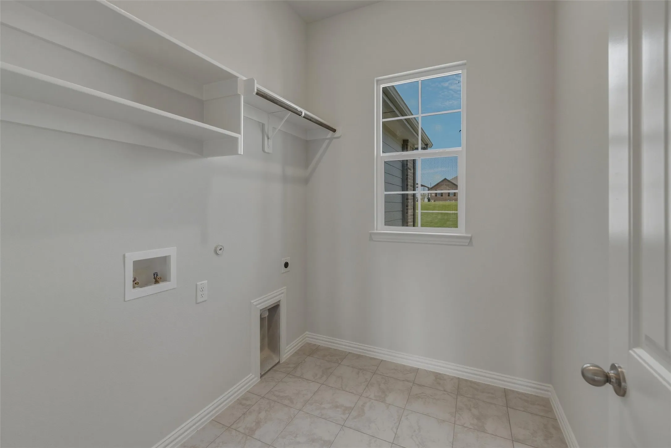 Laundry area featuring wall-mounted shelving, a utility rod, tiled flooring, and a single window