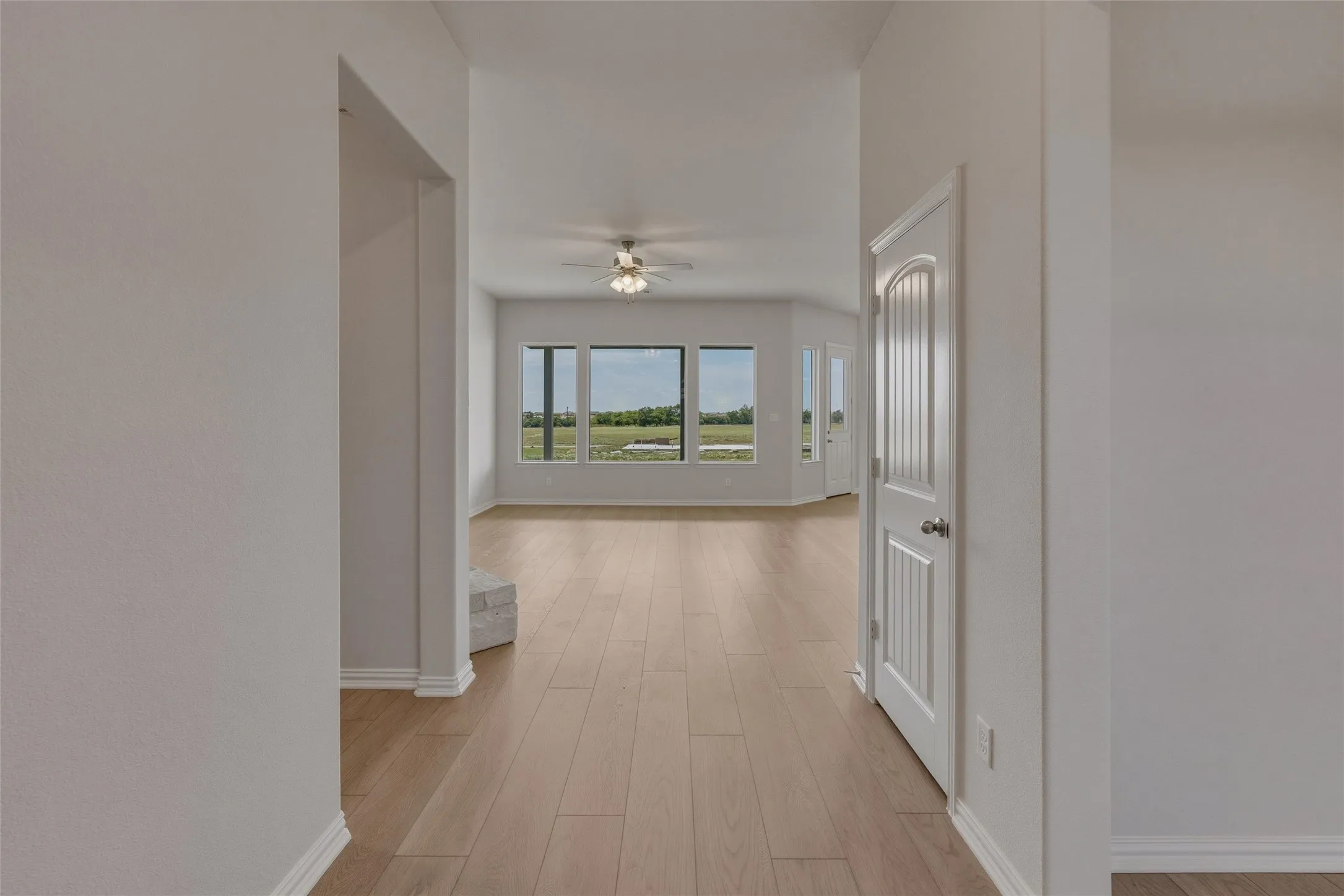 Vaulted ceiling with a ceiling fan, ample natural light through multiple windows, light wood-finish flooring, and a white paneled interior door