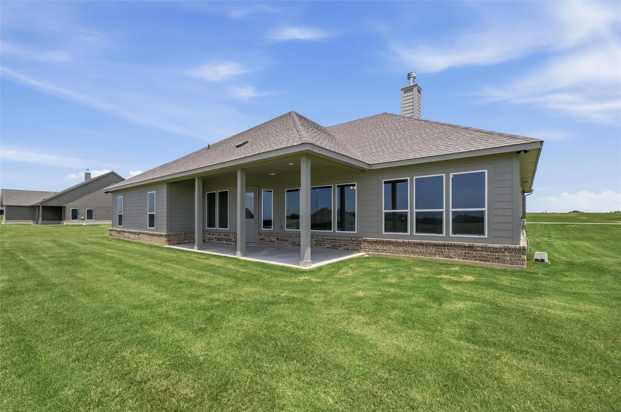 Expansive rear patio with overhead coverage, multiple large windows, and a brick foundation accent
