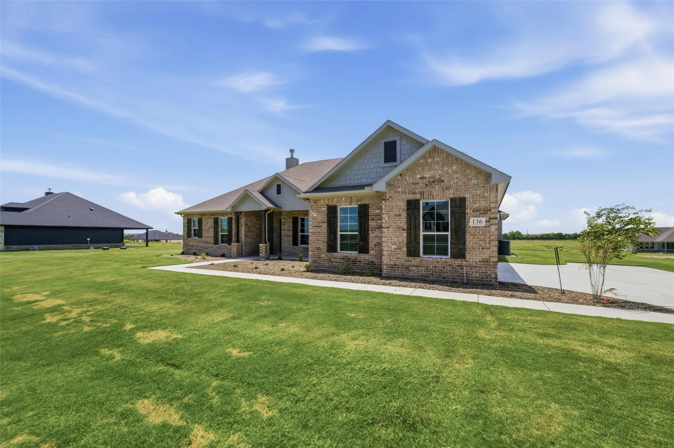 Brick veneer exterior with gabled roofline, dark shutters, and a concrete driveway