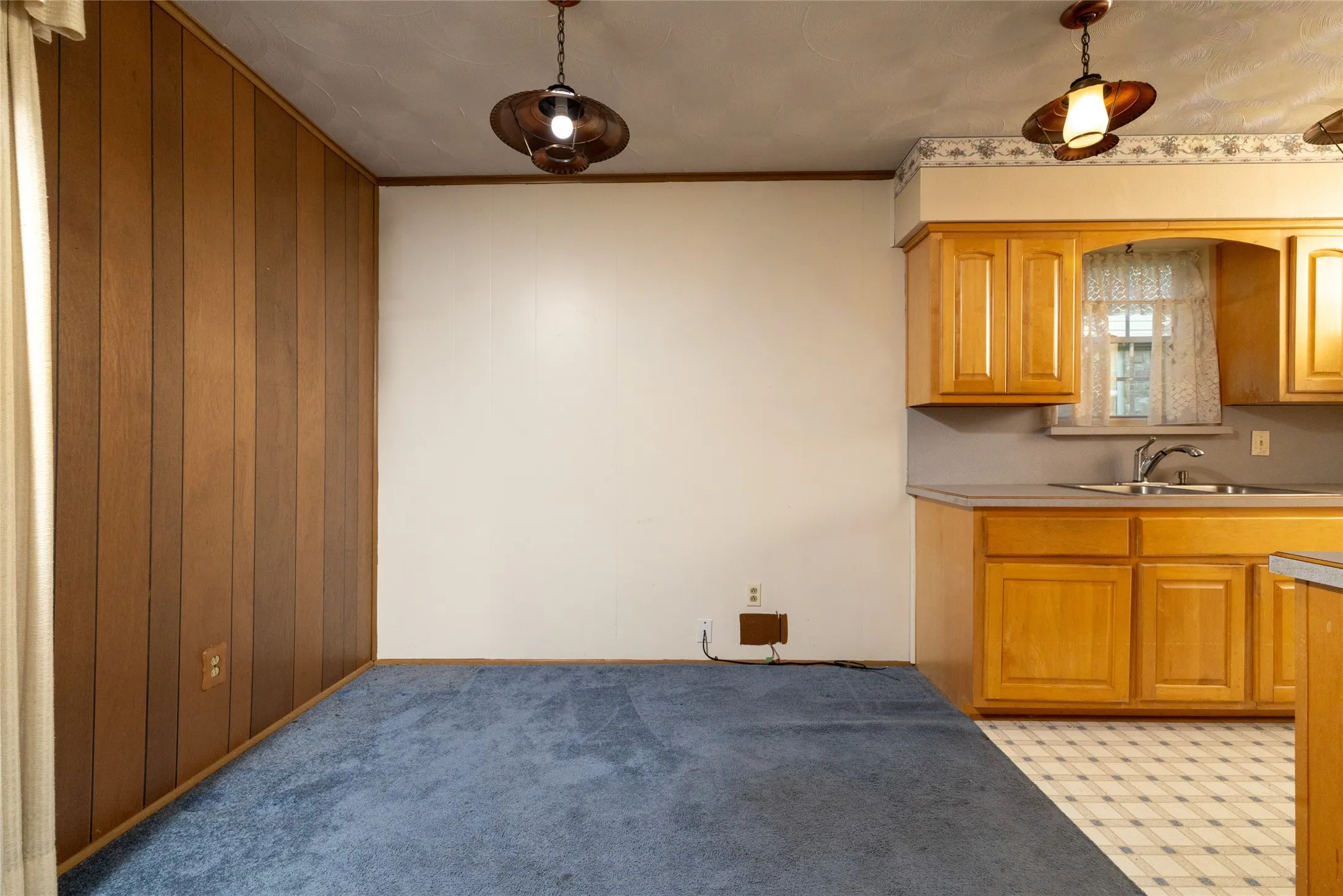 Wood paneling, pendant lighting, light wood cabinetry, laminate countertops, and vinyl tile flooring