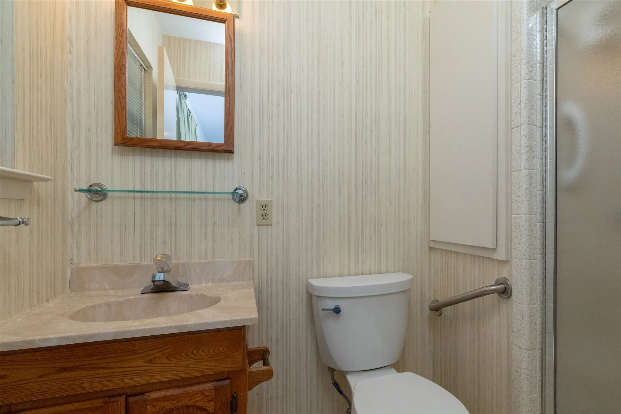 Vanity with integral sink, wood-finish cabinetry, and framed mirror